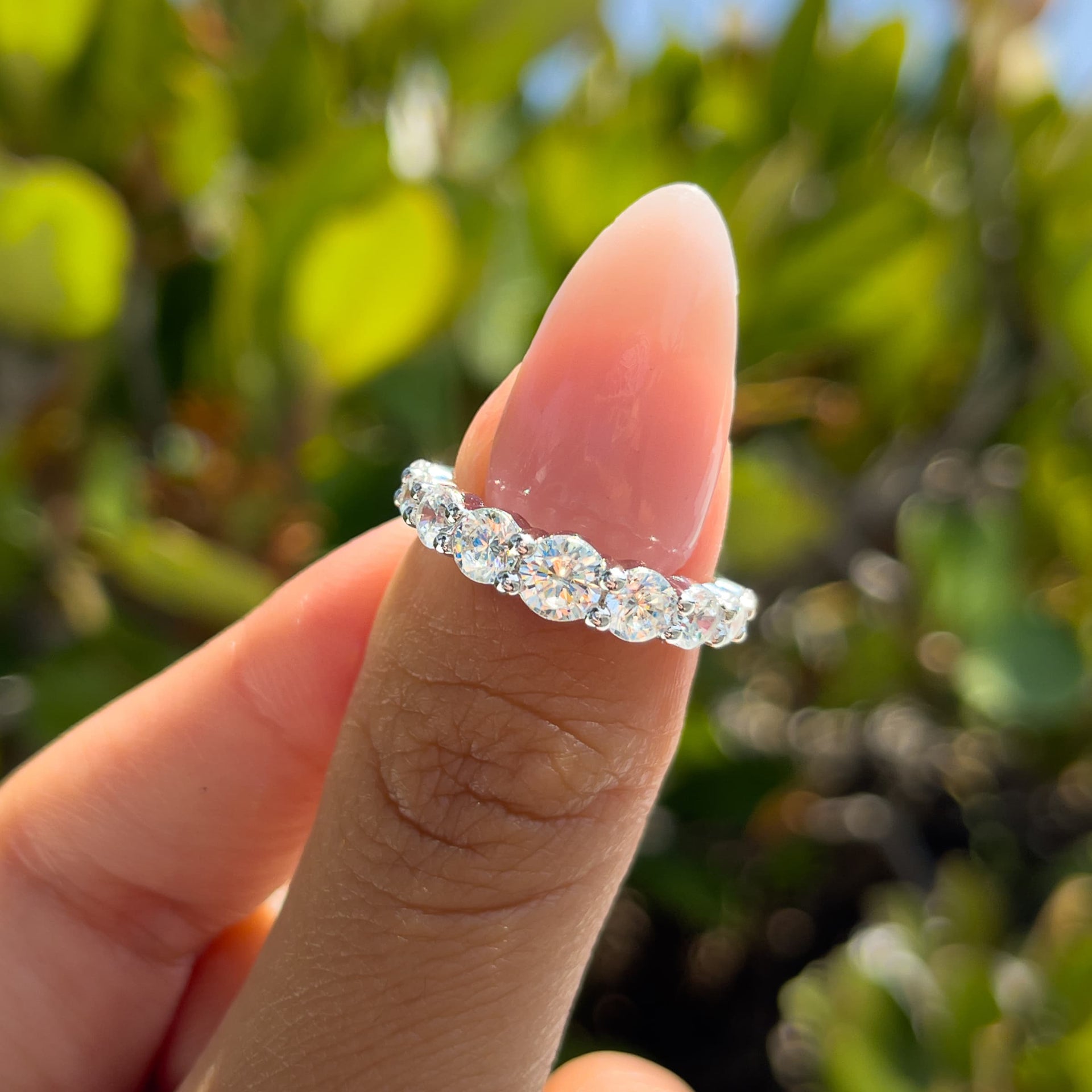 stunning bold silver half eternity wedding band held by model with neutral nails in front of greenery