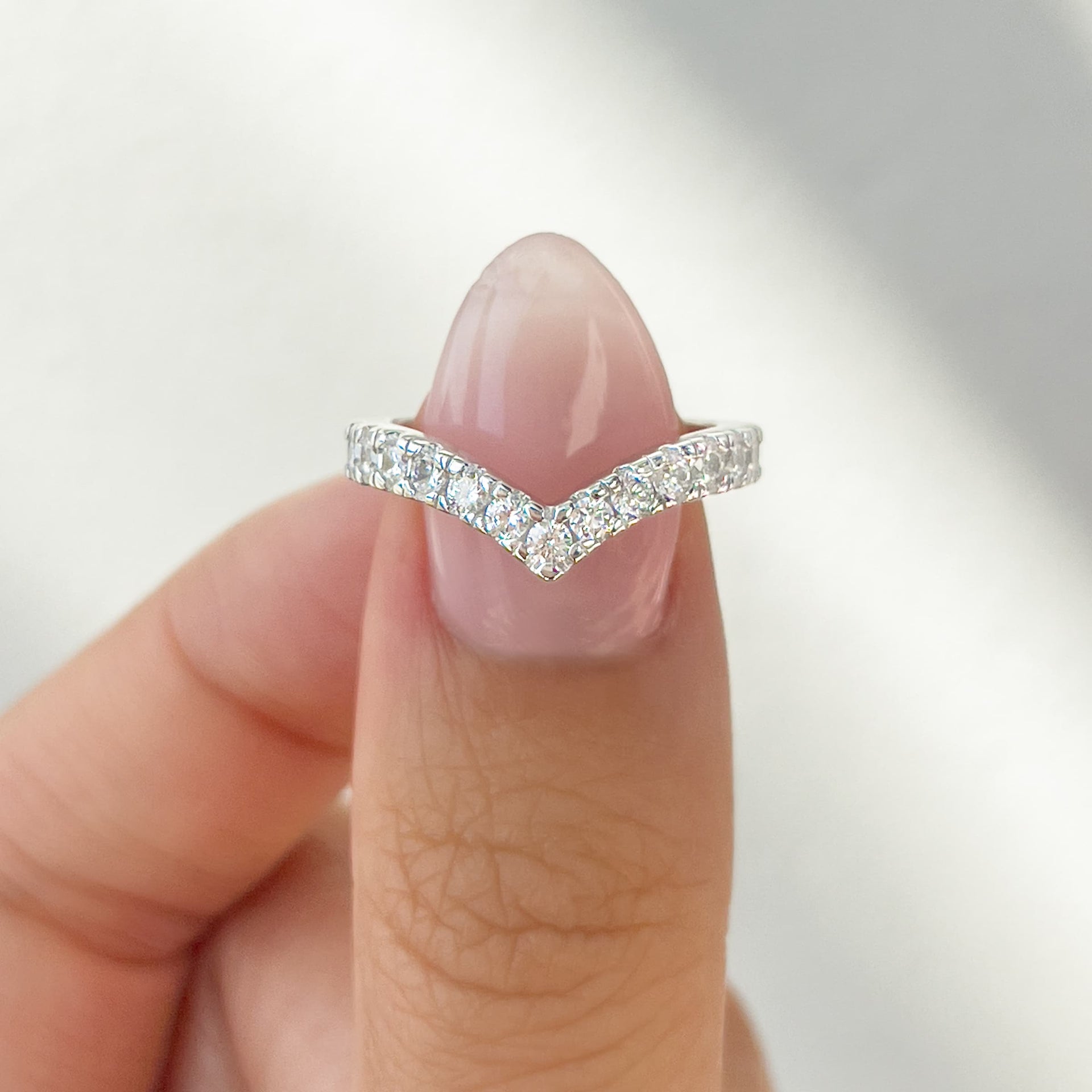simple silver half eternity chevron wedding band held by model with neutral nails