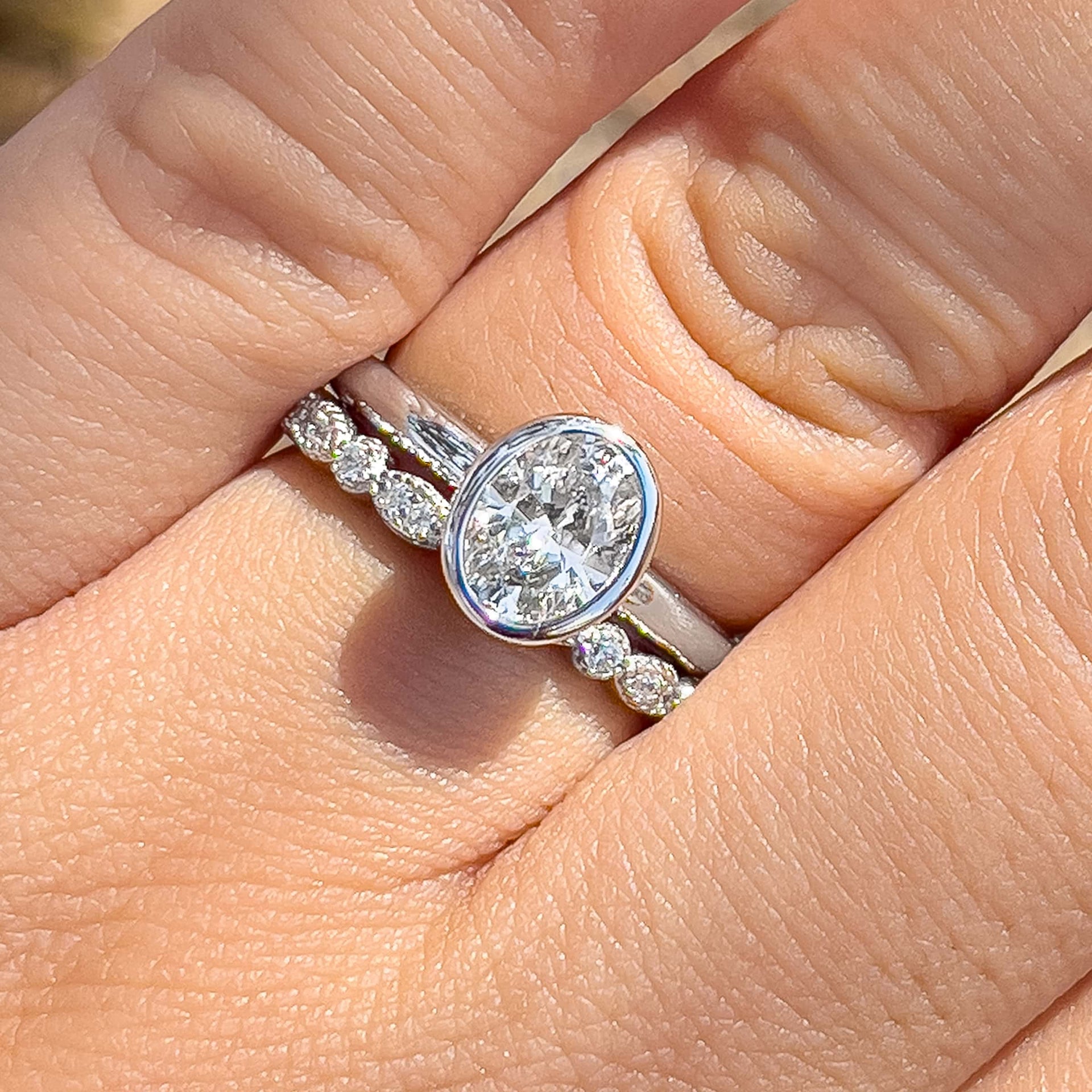 silver oval cut bezel engagement ring on model's ring finger with a paired silver pav wedding band