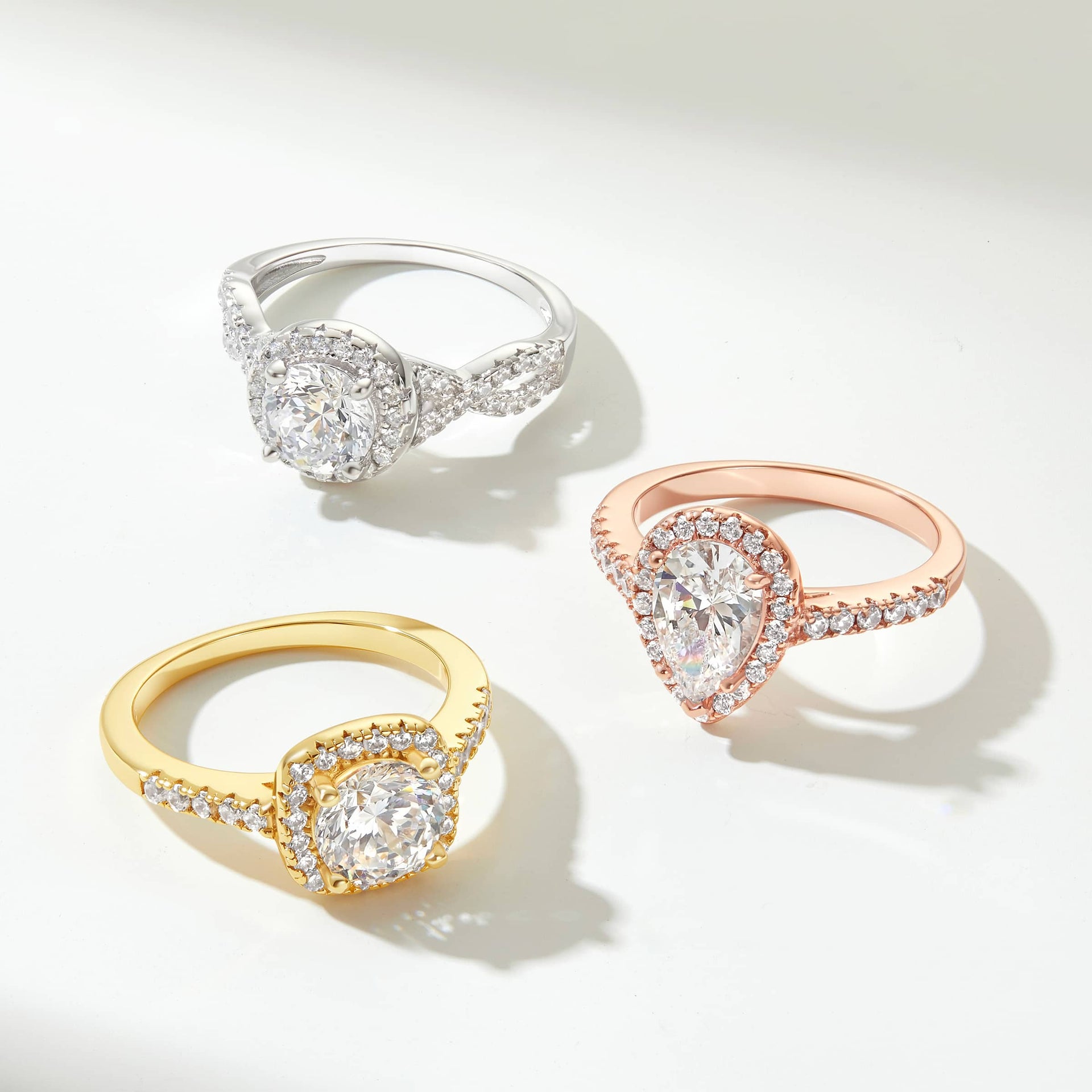 Three engagement rings in silver, gold, and rose gold placed on an off white background