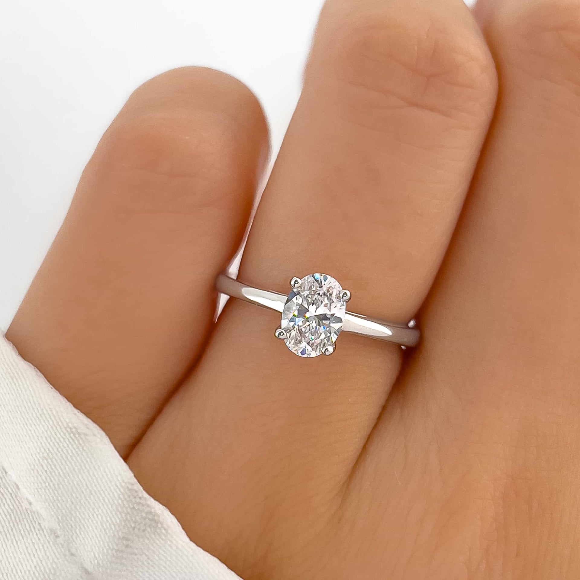 stunning silver petite engagement ring with oval cut on ladies hand with white sleeve