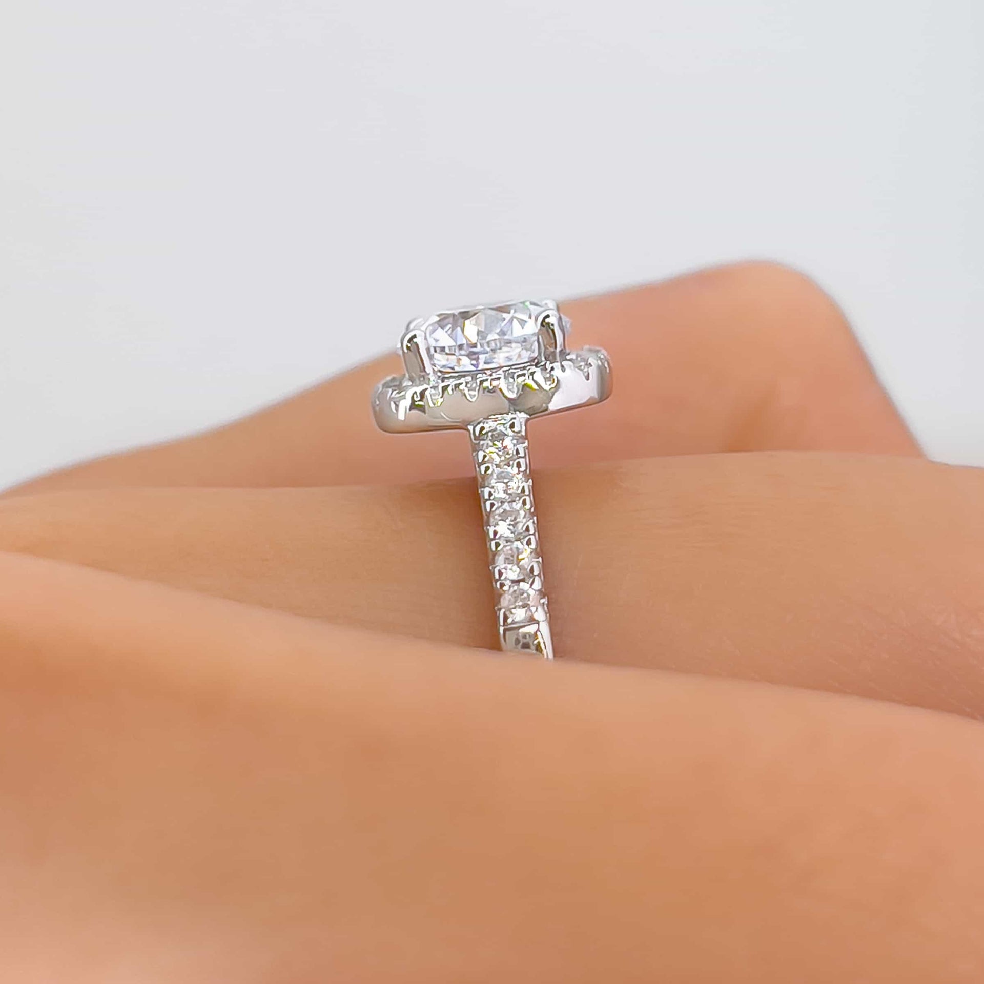Close up side view of The Evermore silver engagement ring with 1.5 carat round-cut simulated diamond with a raised cushion halo setting and half eternity band