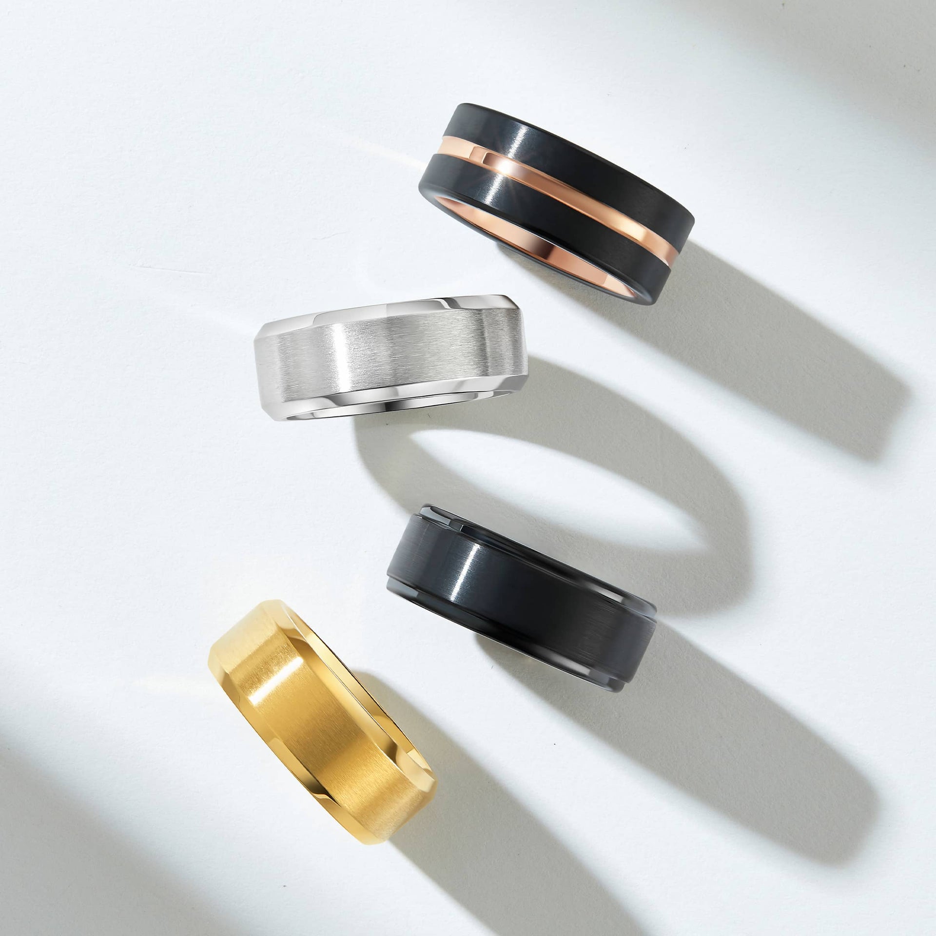 a flat lay showcasing a black and rose gold wedding ring, a silver wedding ring, a black wedding ring, and a gold wedding ring