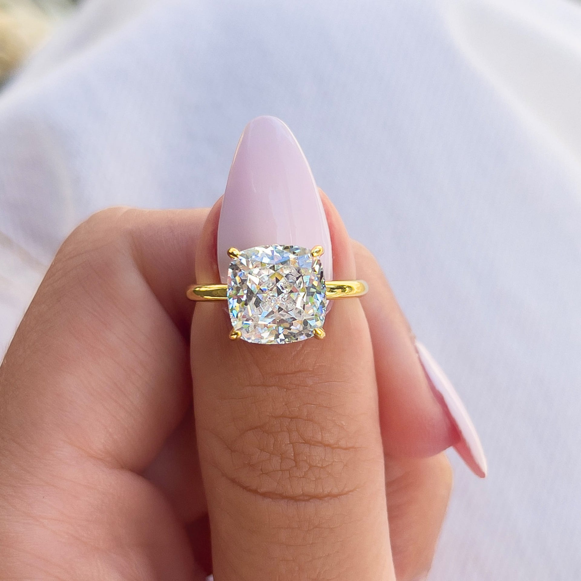 bold 3.5 carat cushion cut solitaire with hidden halo detail on female model with a light pink nail