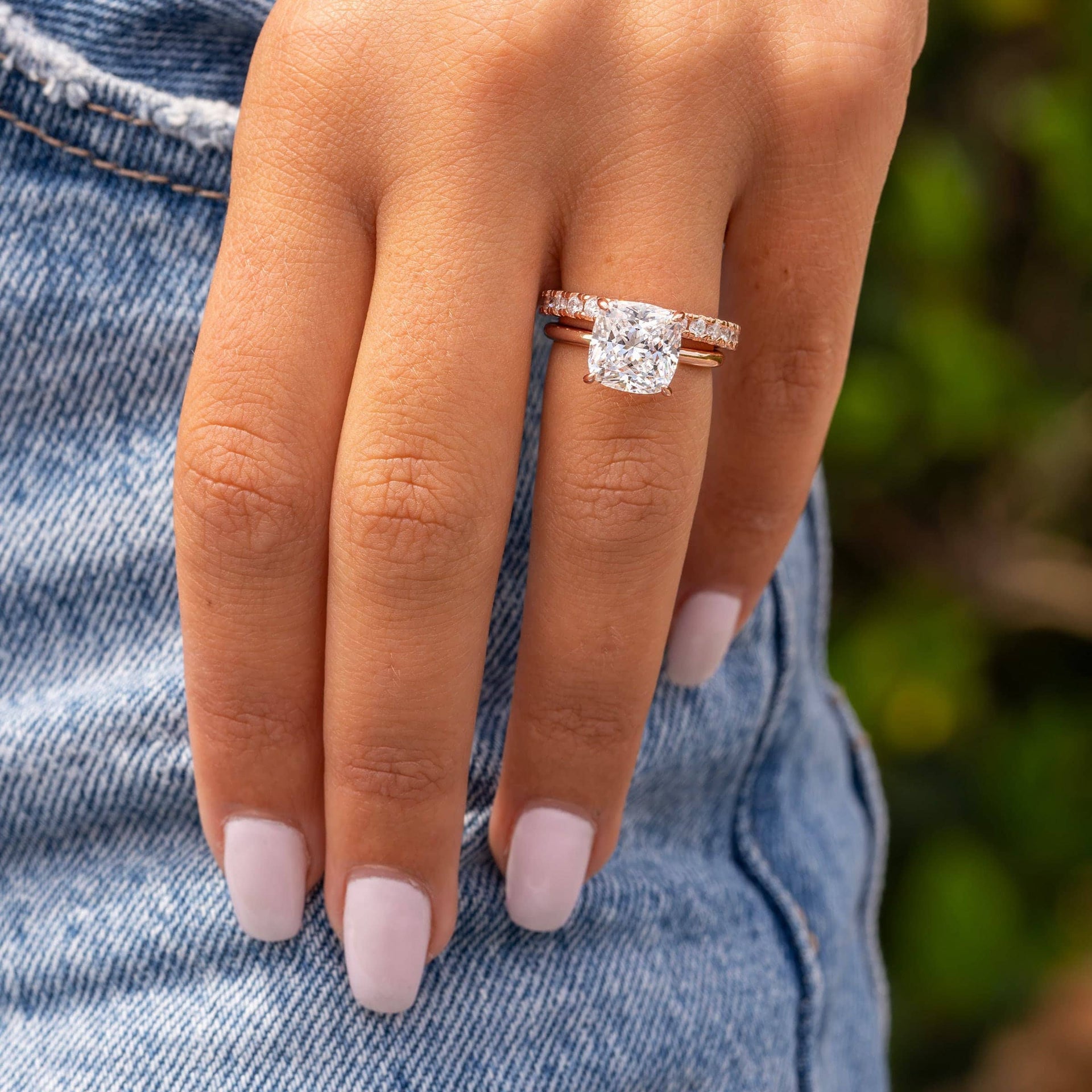 The Claire rose gold engagement ring with 3.5 carat cushion-cut simulated diamond solitaire stacked with eternity band, shown on hand against denim