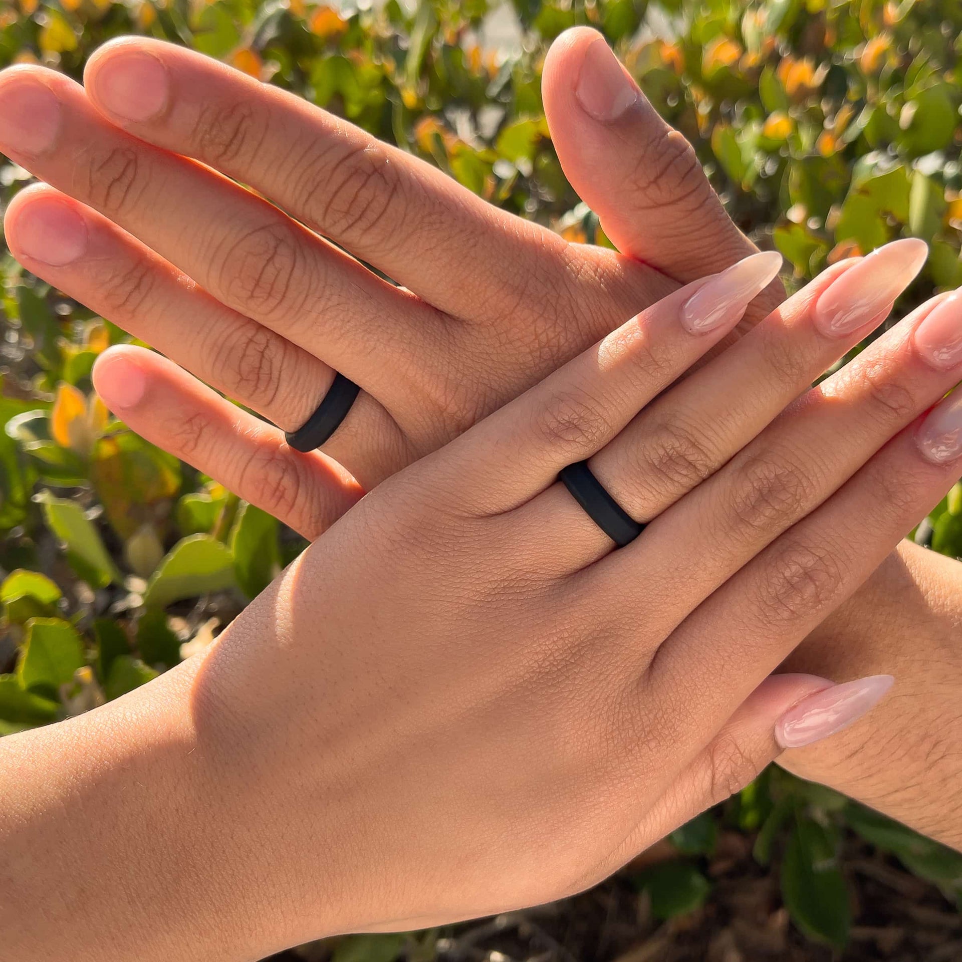 black unisex silicone wedding band shown worn by a male and female model in front of some greenery