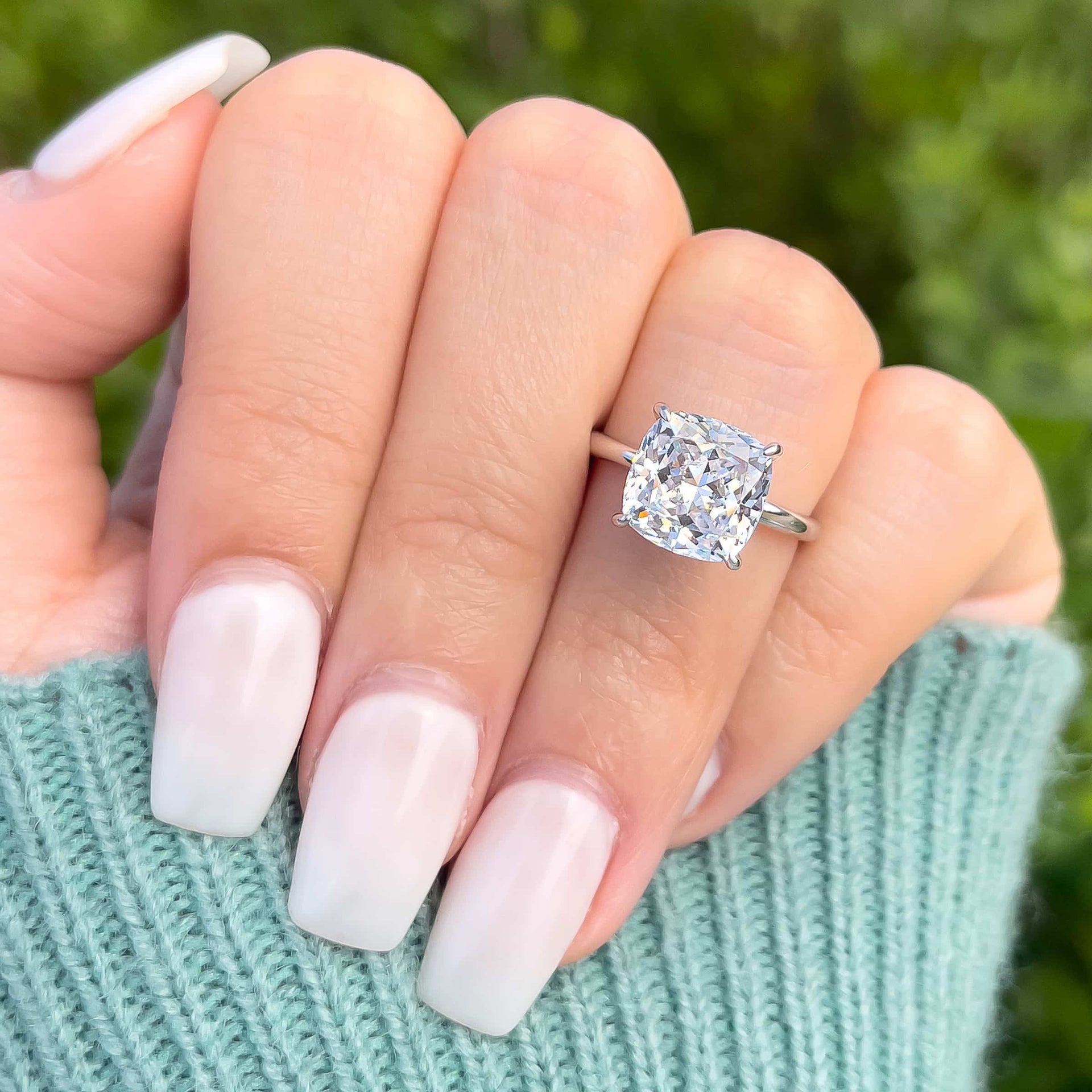 Close-up of The Claire silver engagement ring with 3.5 carat cushion-cut simulated diamond solitaire, worn with square white acrylic nails
