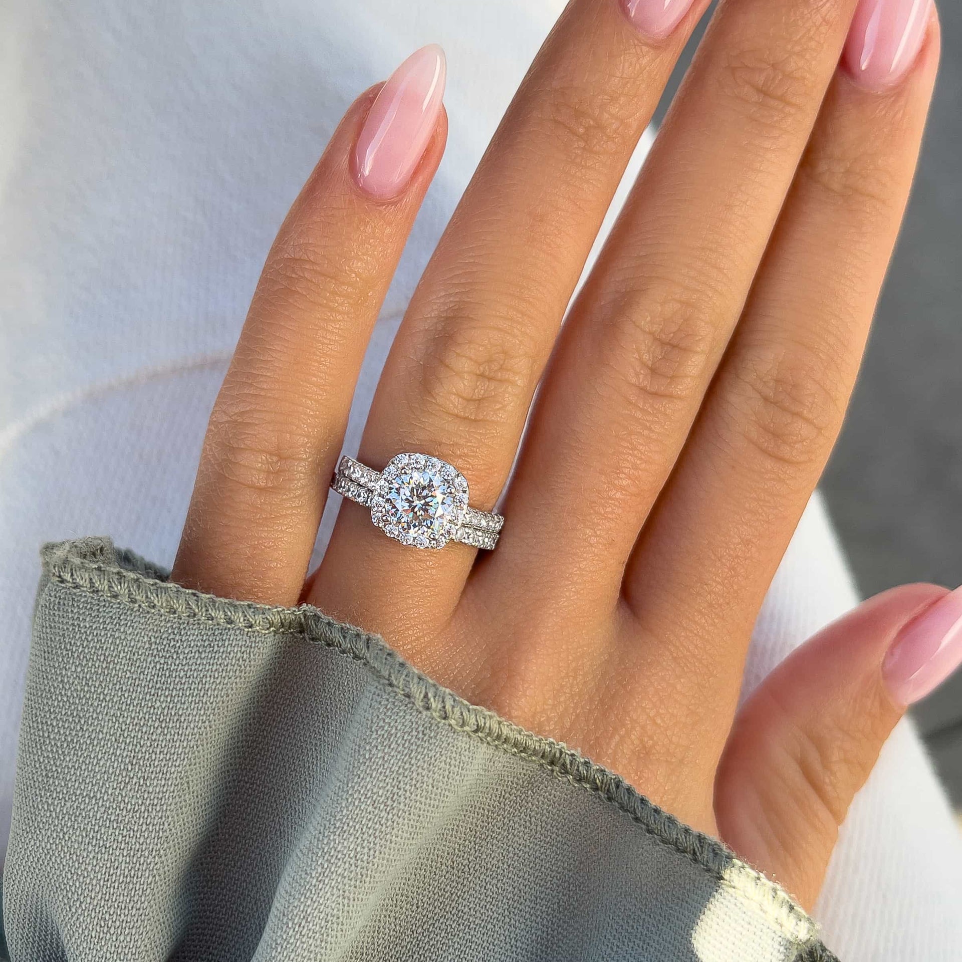 Silver engagement ring set with 1.5 carat round-cut simulated diamond in a cushion halo, paired with matching pavé wedding band on a woman’s hand