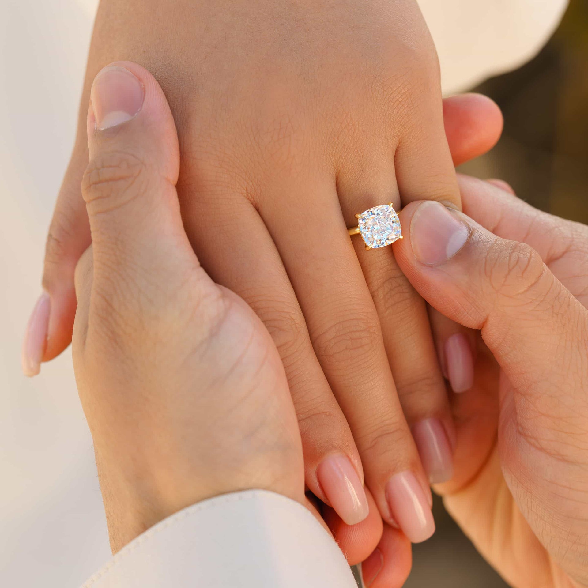Couple holding hands during proposal with The Claire gold engagement ring featuring 3.5 carat cushion-cut simulated diamond and hidden halo