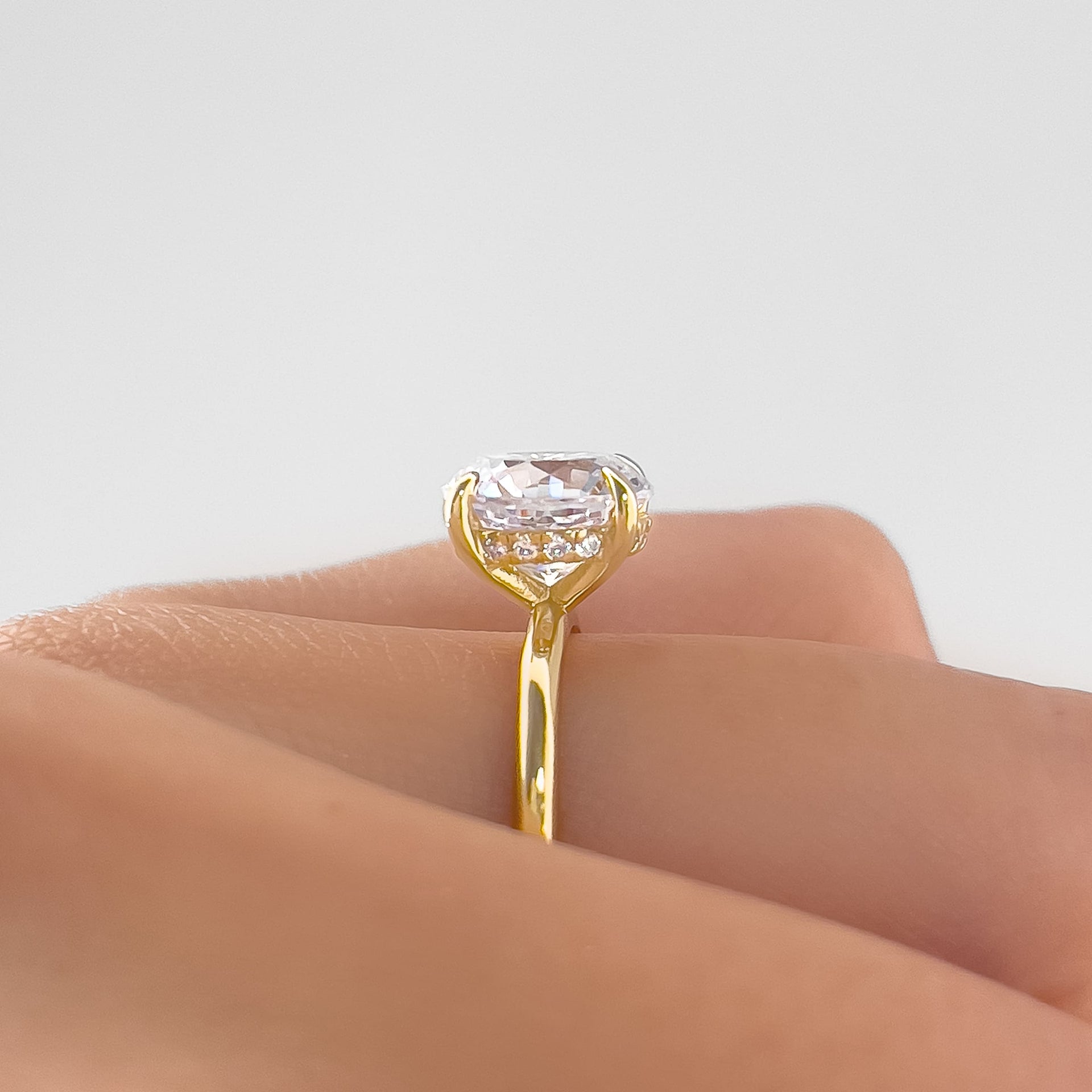 Side view of The Claire gold engagement ring with 3.5 carat cushion-cut simulated diamond and hidden halo setting on white background