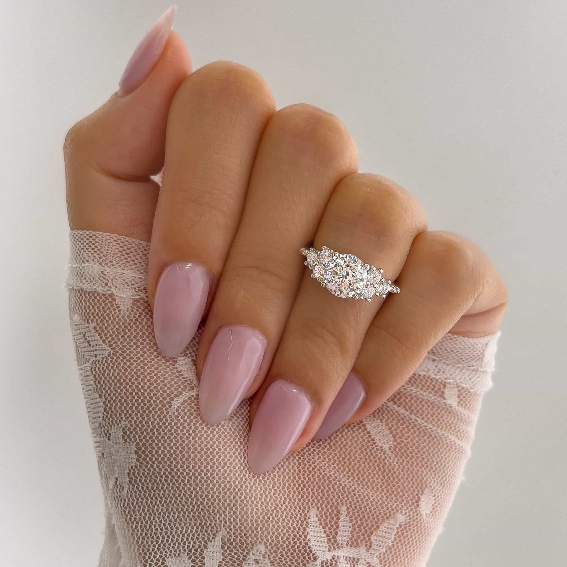 unique silver round cut engagement ring held by model with light pink nails