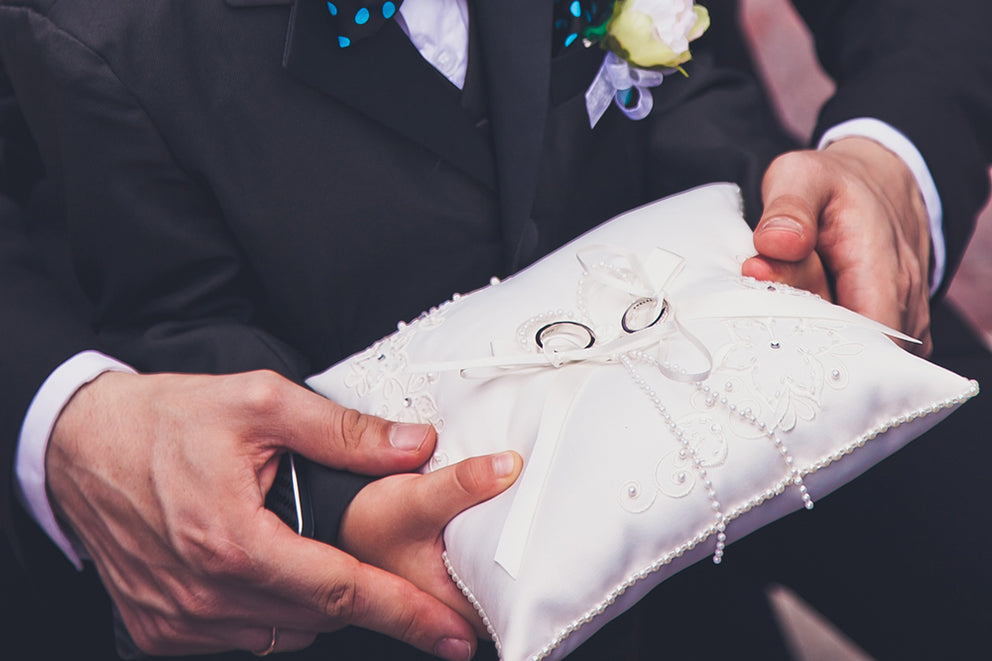 a close up of a man helping a ringbearer hold the pillow with the wedding rings