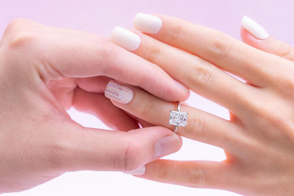 a close up of a man putting a solitaire engagement on a womans hand