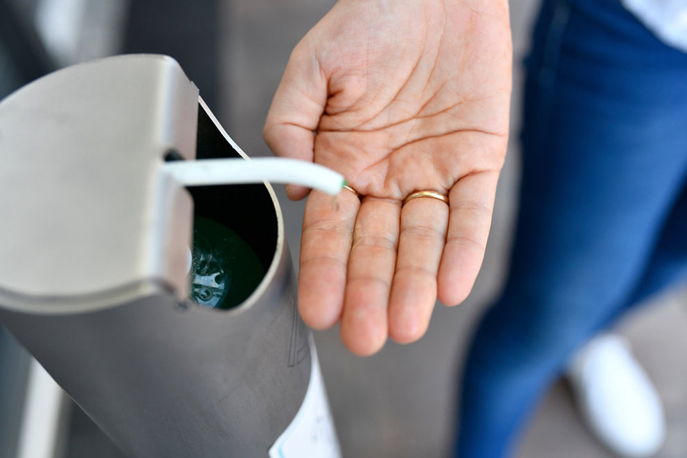 a person using an automated hand sanitizer dispenser