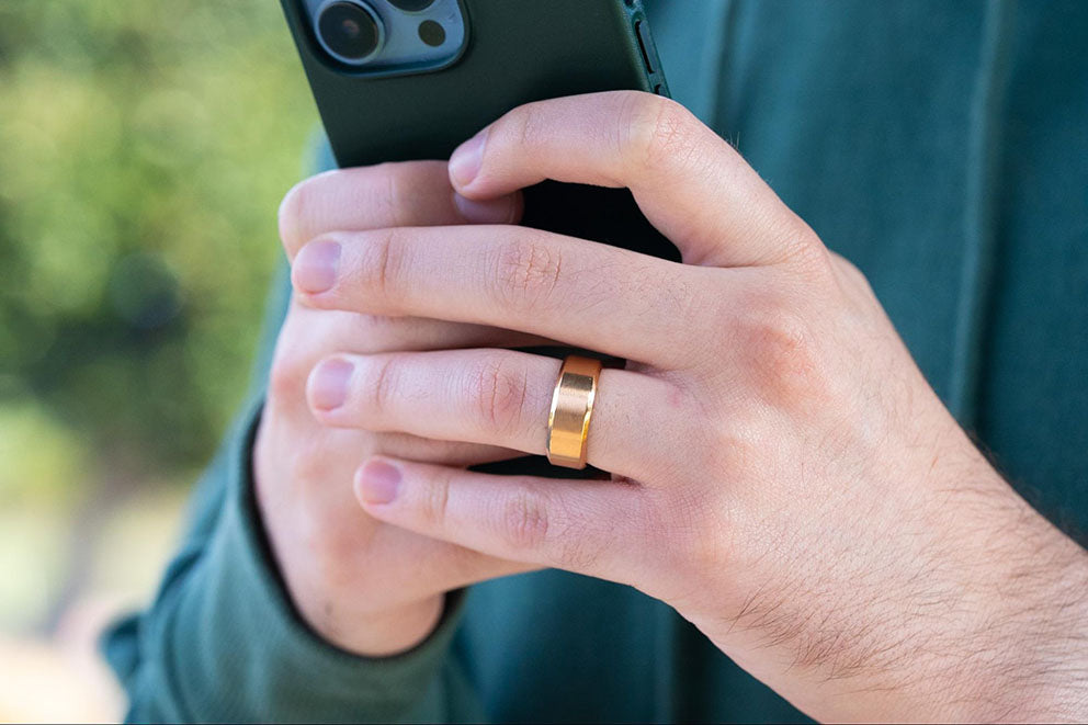 a man holding his phone while wearing a gold colored titanium wedding band