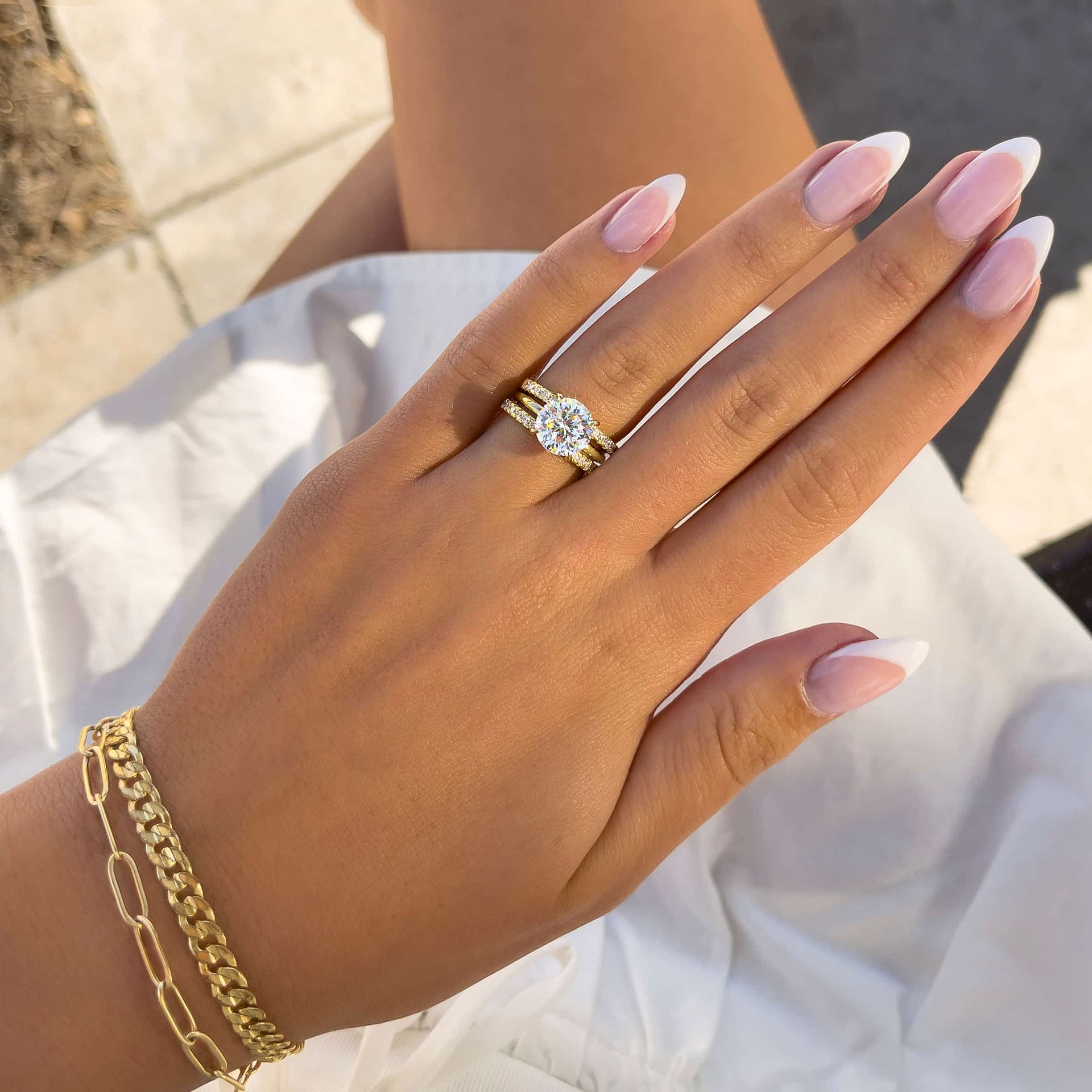 Gold 3 carat round cut solitaire engagement ring with two complementary gold wedding bands on model in white dress with french tip nails