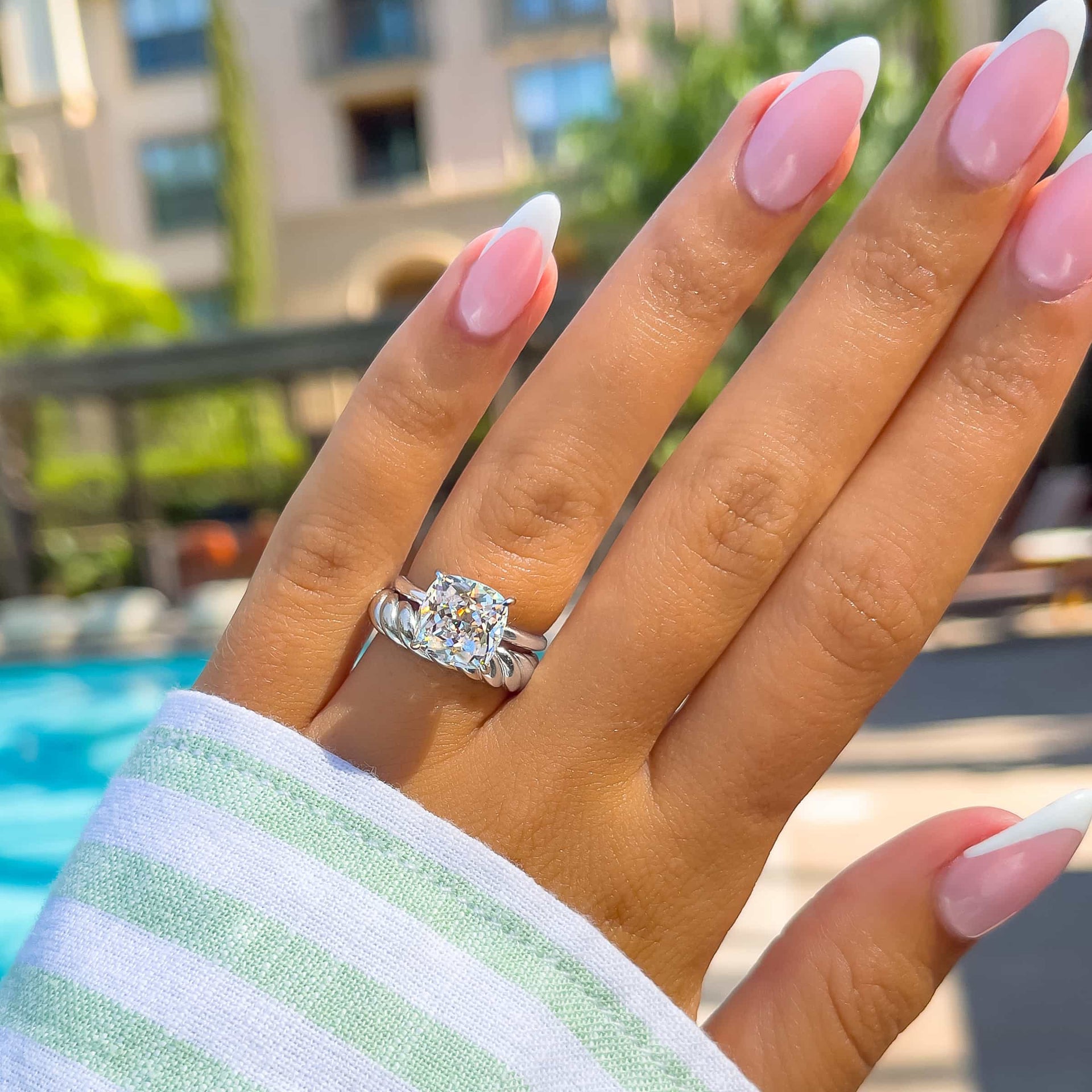 gorgeous silver wedding ring set made up of cushion cut solitaire ring and thick twisting-style wedding band on model with french tip nails