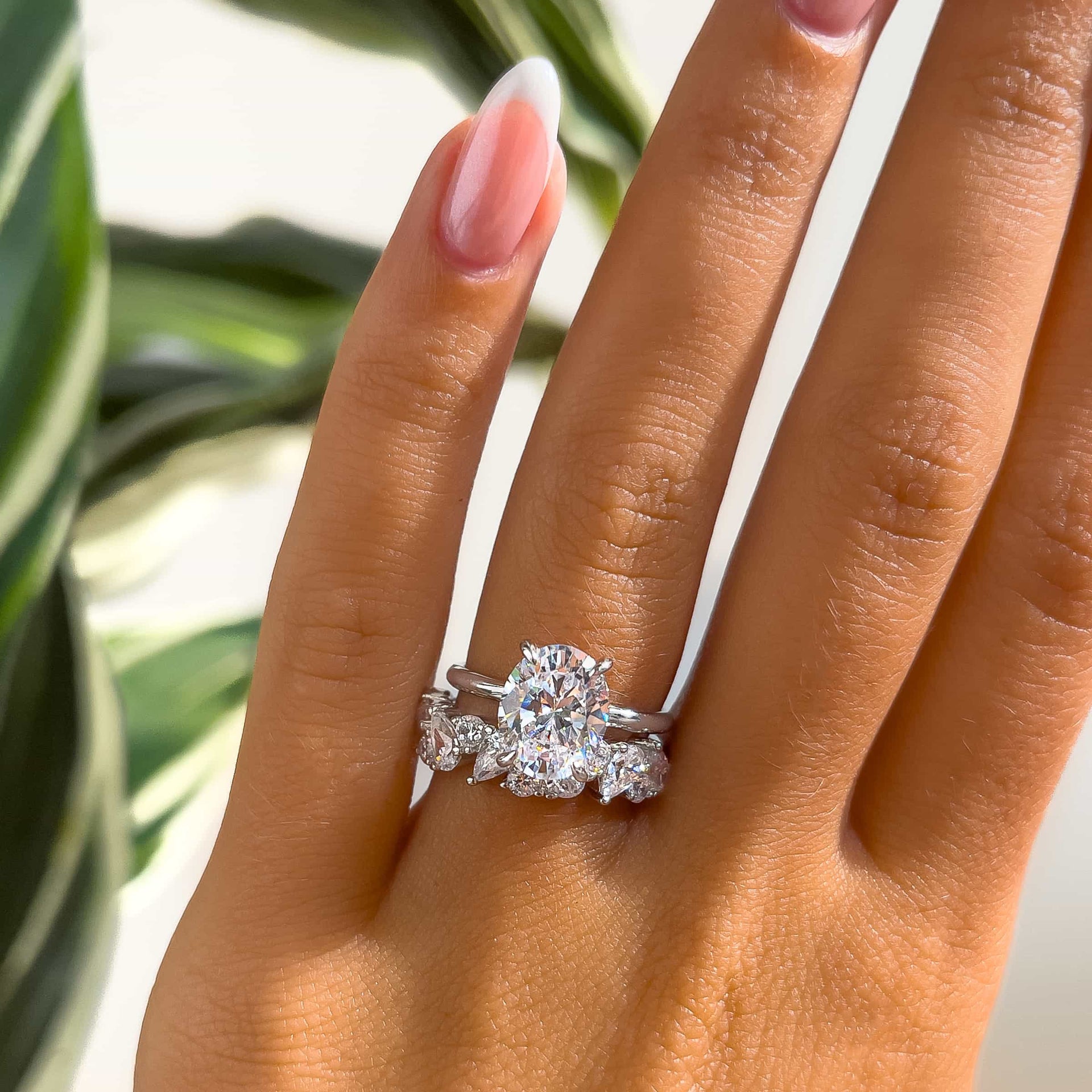 gorgeous silver oval cut solitaire paired with bold mixed cut wedding band on model in front of plant