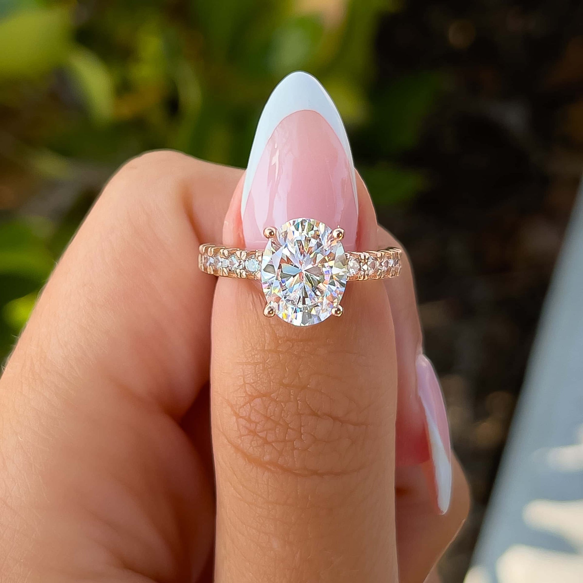 rose gold oval cut engagement ring with thicker half eternity band detailing on model with french tip nails