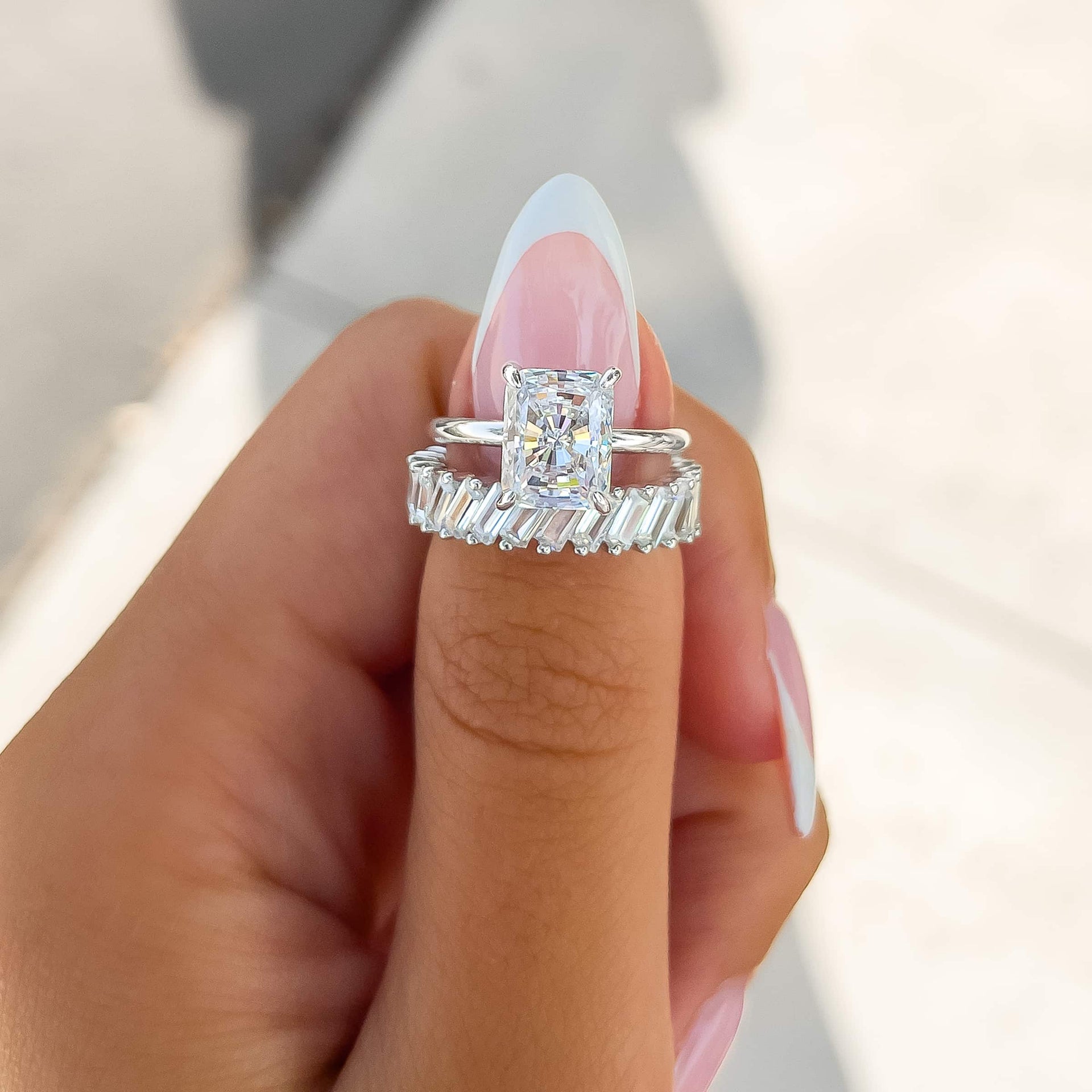 classic silver 3 carat radiant cut solitaire engagement ring paired with silver baguette band on model with french tip nails