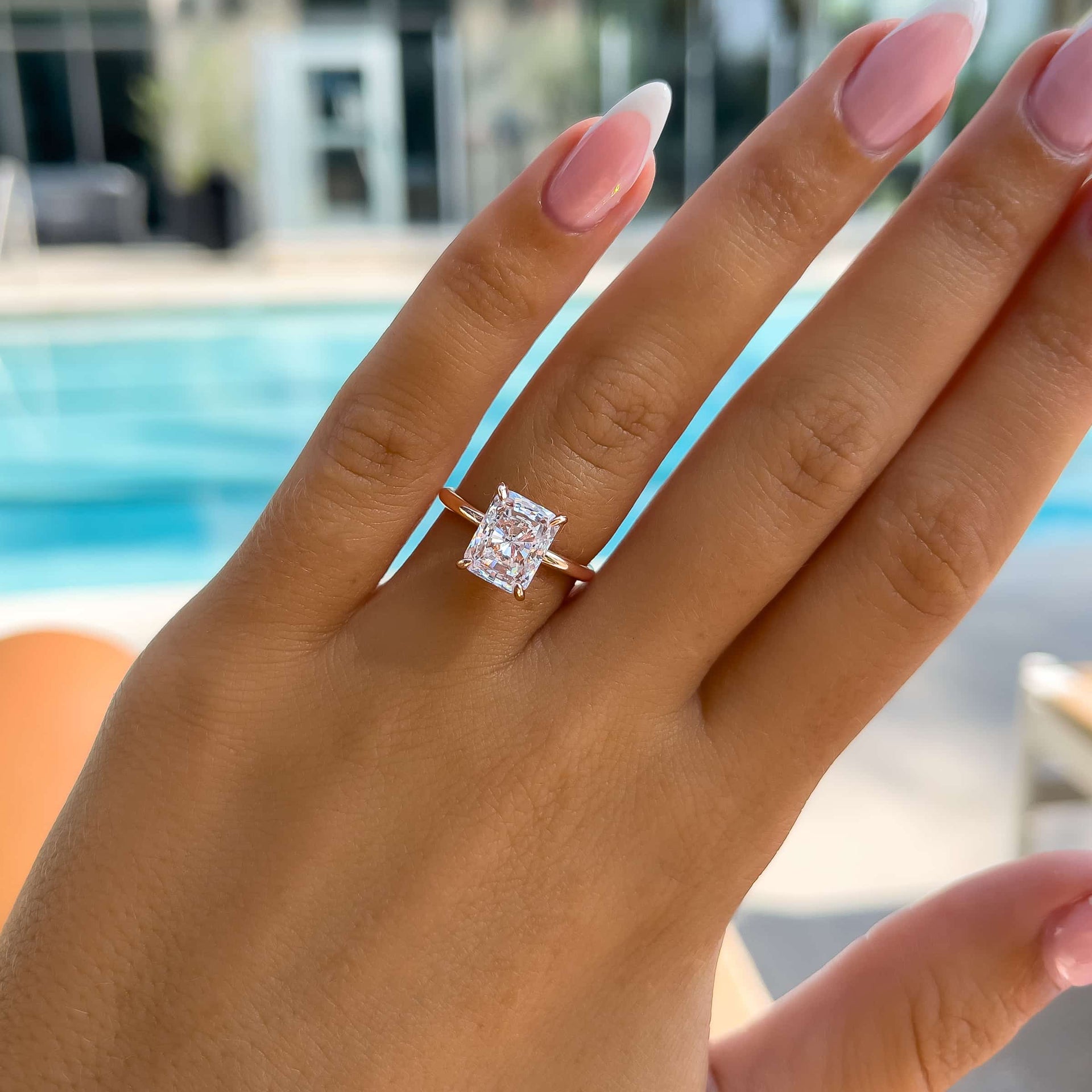 stunning rose gold 3 carat radiant cut solitaire engagement ring on model with french tip nails in front of pool