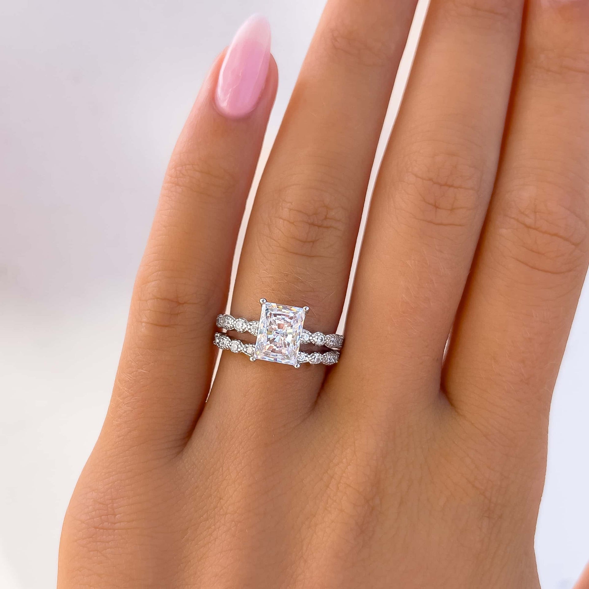 silver 1.5 carat radiant cut engagement ring paired with a matching silver band on model with light pink nails