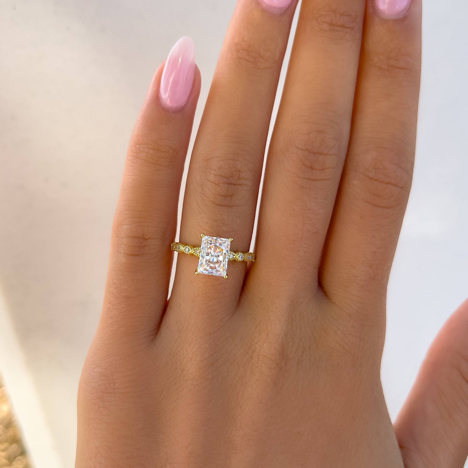 gold radiant cut engagement ring on model with light pink nails