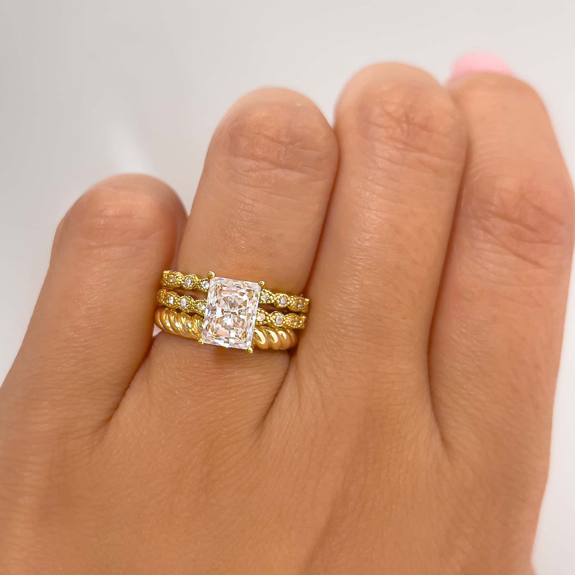 gold triple wedding ring stack featuring a radiant cut engagement ring and two different gold wedding bands