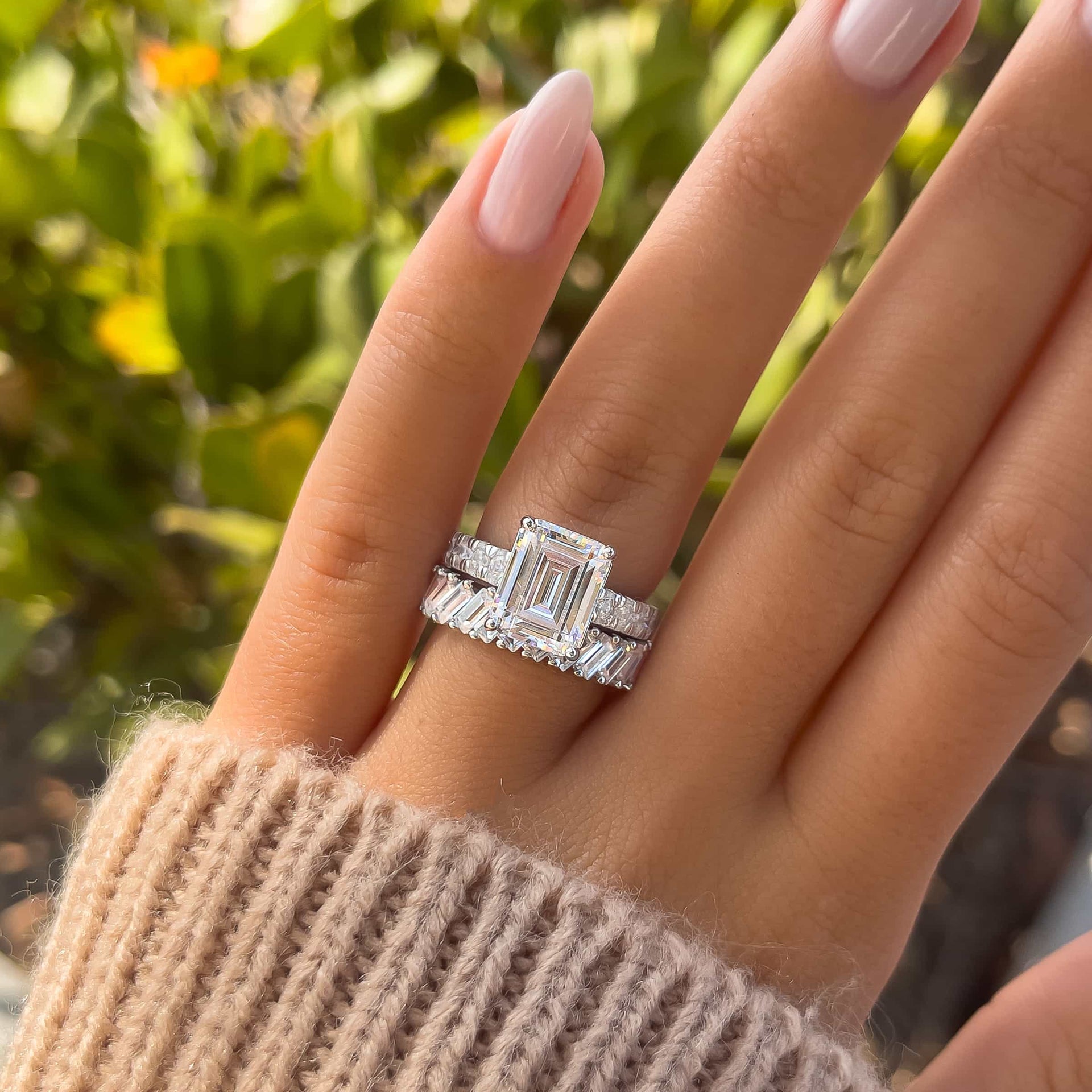 silver 3.75 carat emerald cut engagement ring paired with unique silver baguette band on model with neutral nails and tan sweater