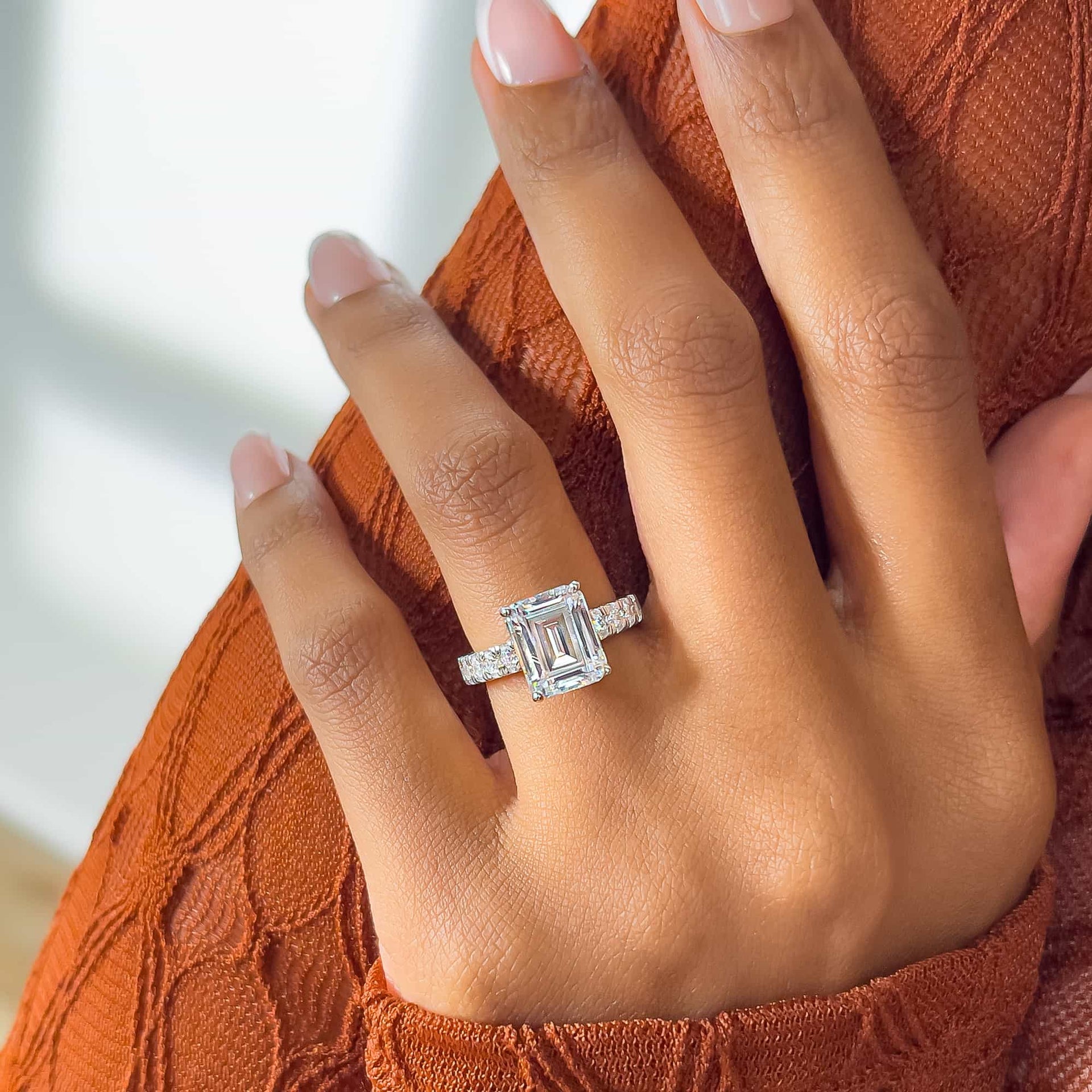 dazzling silver large emerald cut engagement ring with half eternity band detailing on model with french tip nails and orange sweater