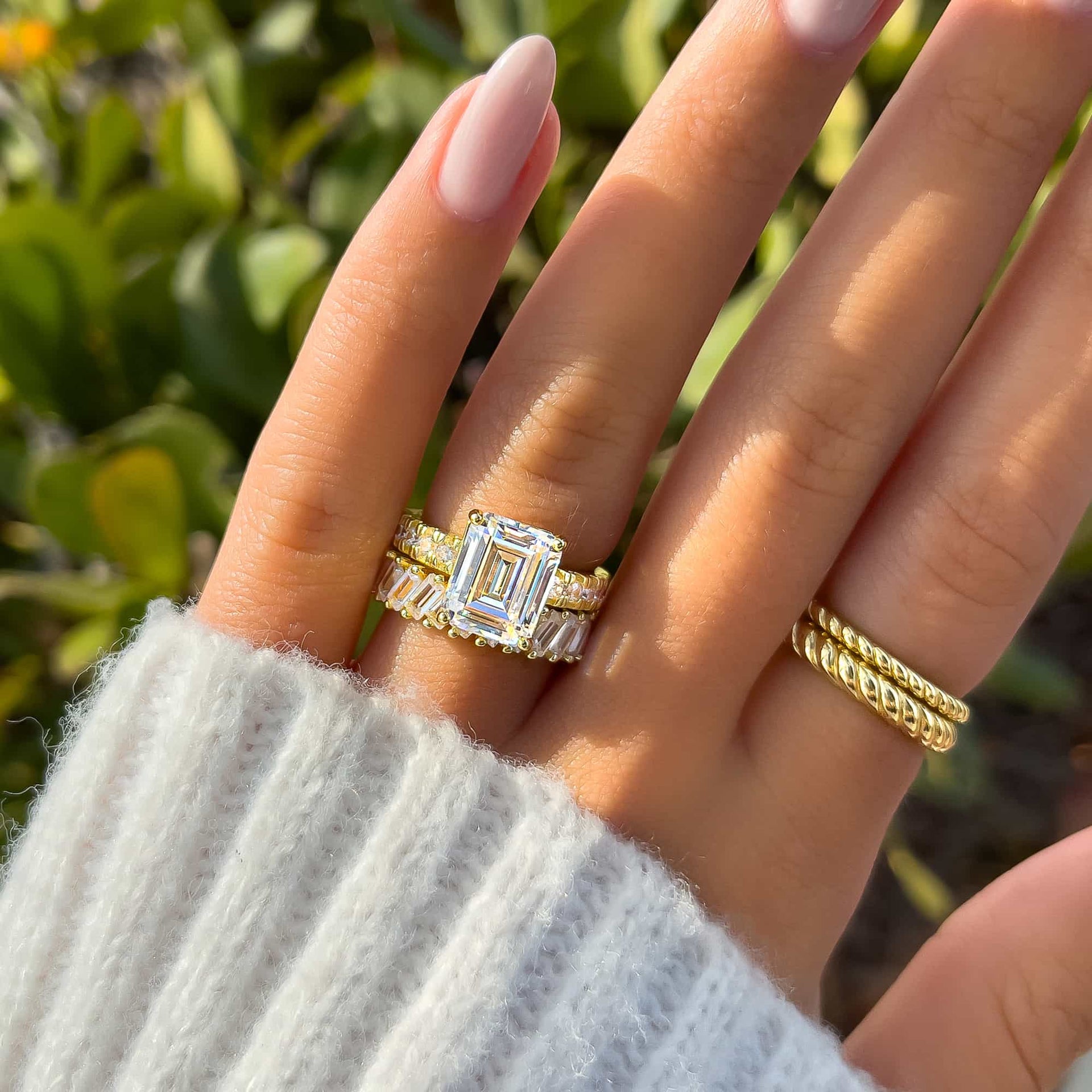 gold emerald cut half eternity engagement ring paired with gold baguette band on model with neutral nails and white sweater