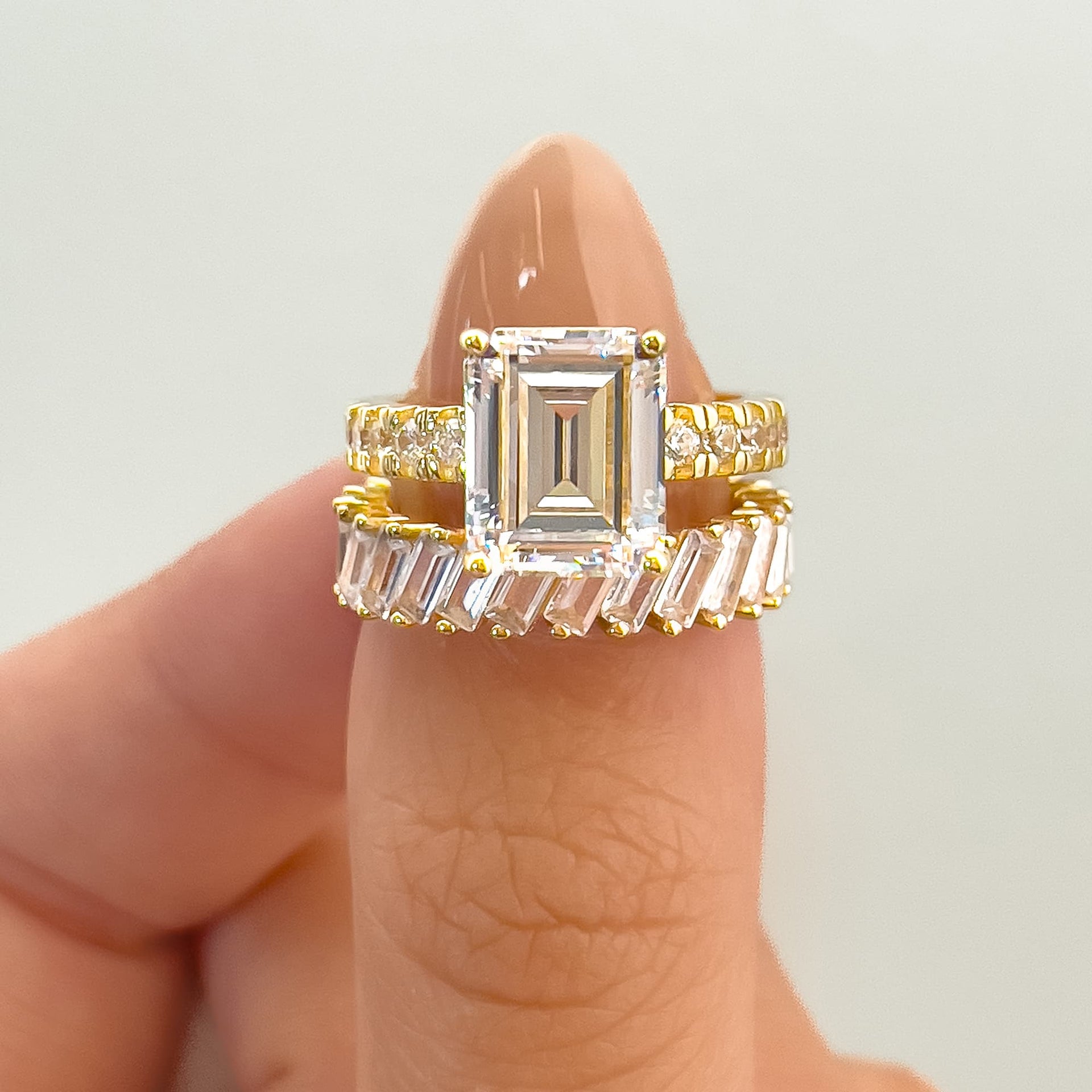 gold 3.75 carat emerald cut half eternity engagement ring paired with baguette wedding band on model with neutral nails