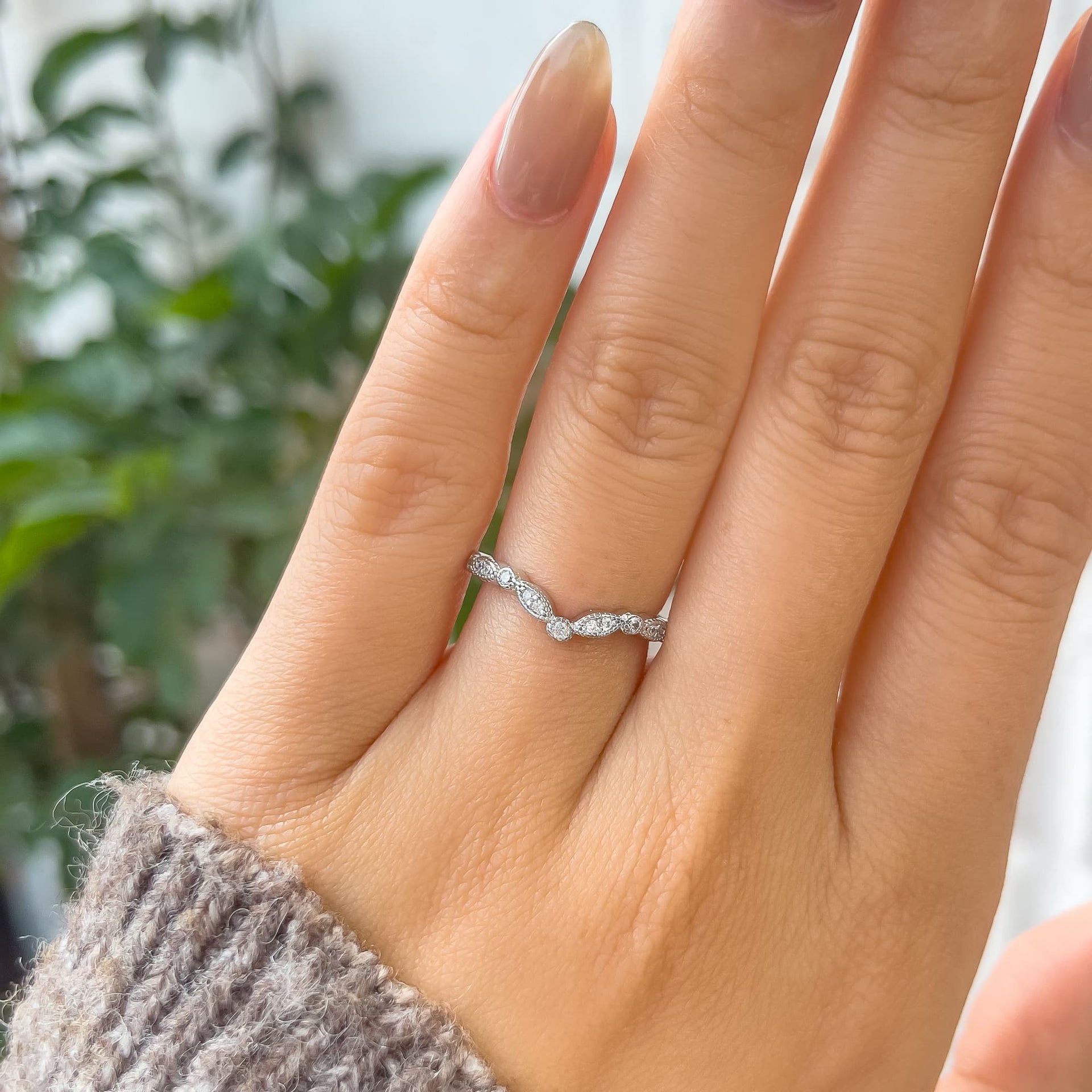 stunning silver chevron wedding band shown on model's hand with brown sweater sleeve and greenery in the background