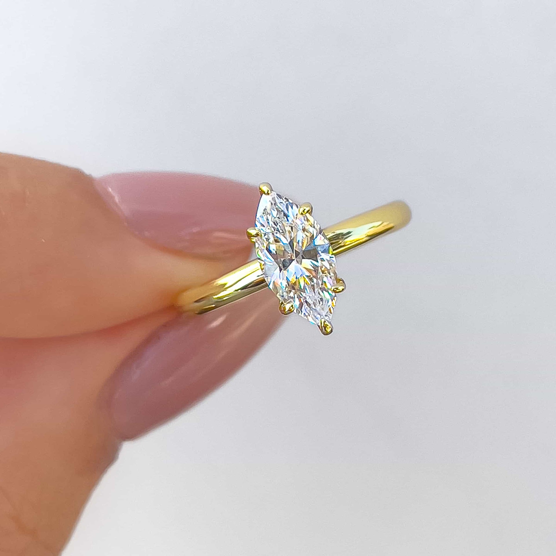 Close up of gold marquise cut solitaire ring held by model with neutral nails