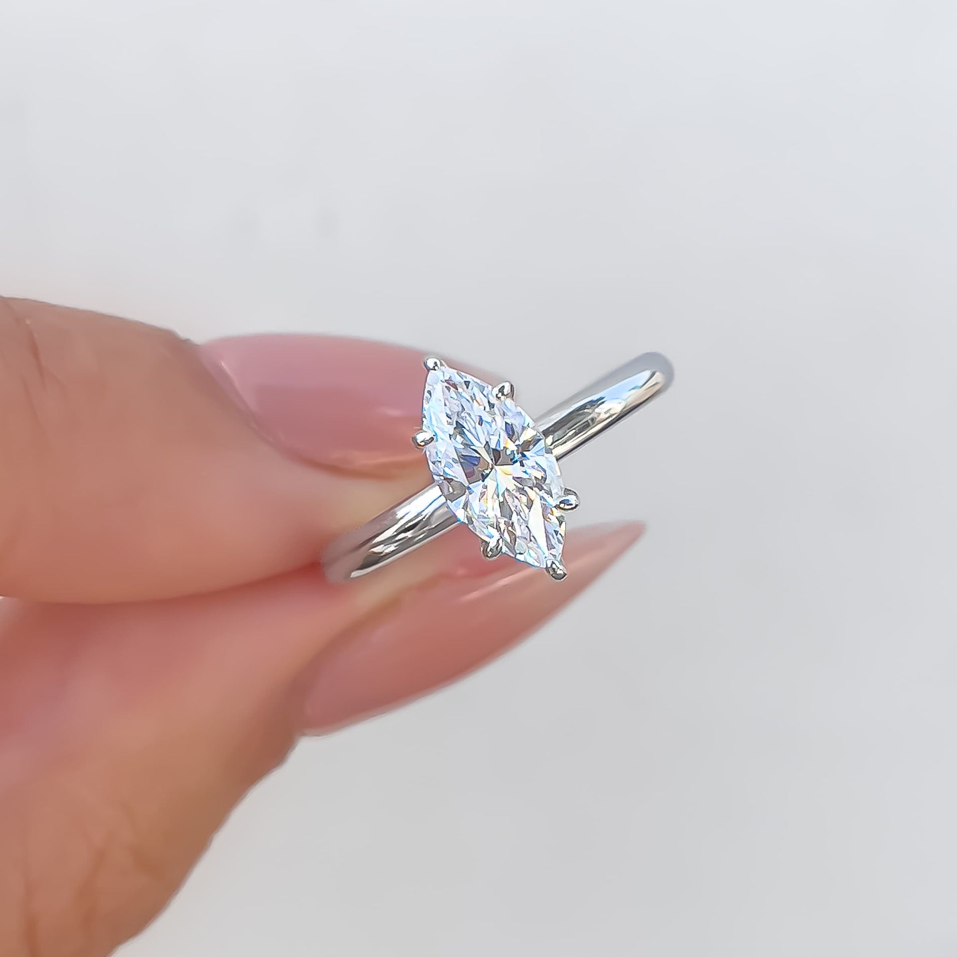 Close up of silver marquise cut solitaire ring held by model with neutral nails