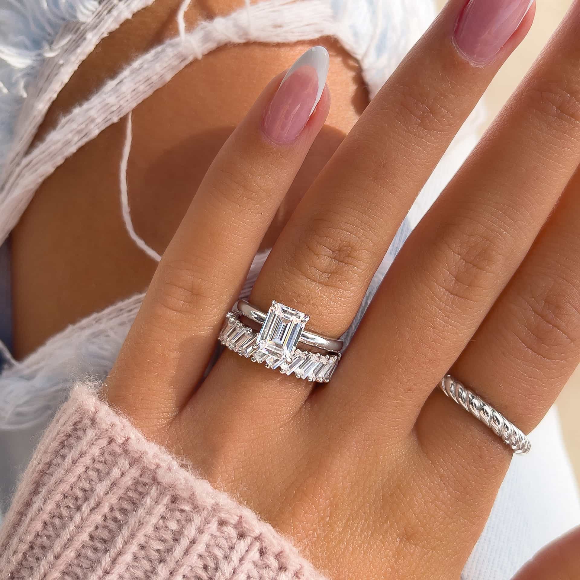 silver wedding ring set made up of an emerald cut solitaire engagement ring and bold baguette wedding band on model with french tip nails