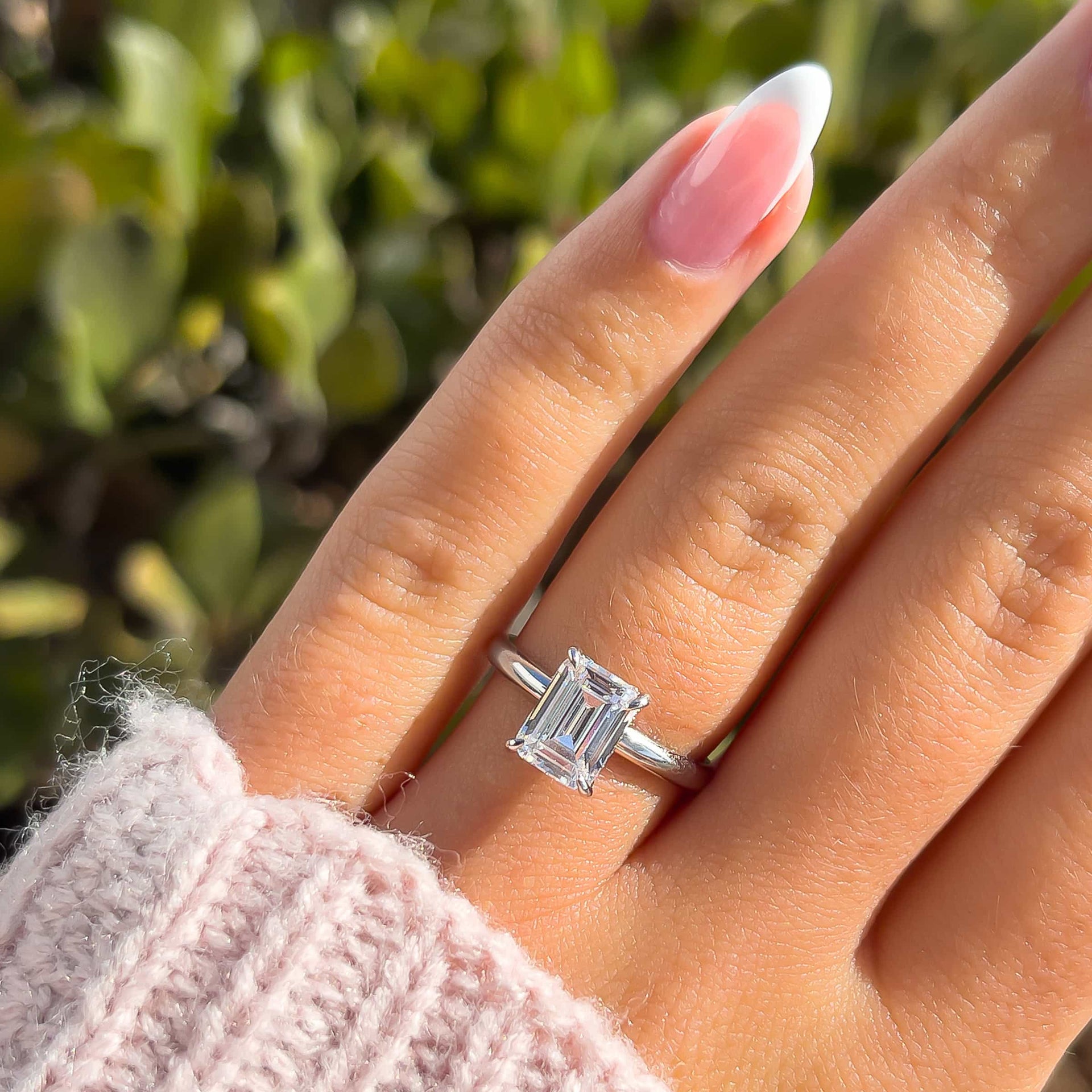 silver 1.5 carat emerald cut engagement ring on model with french tip nails and light pink sweater