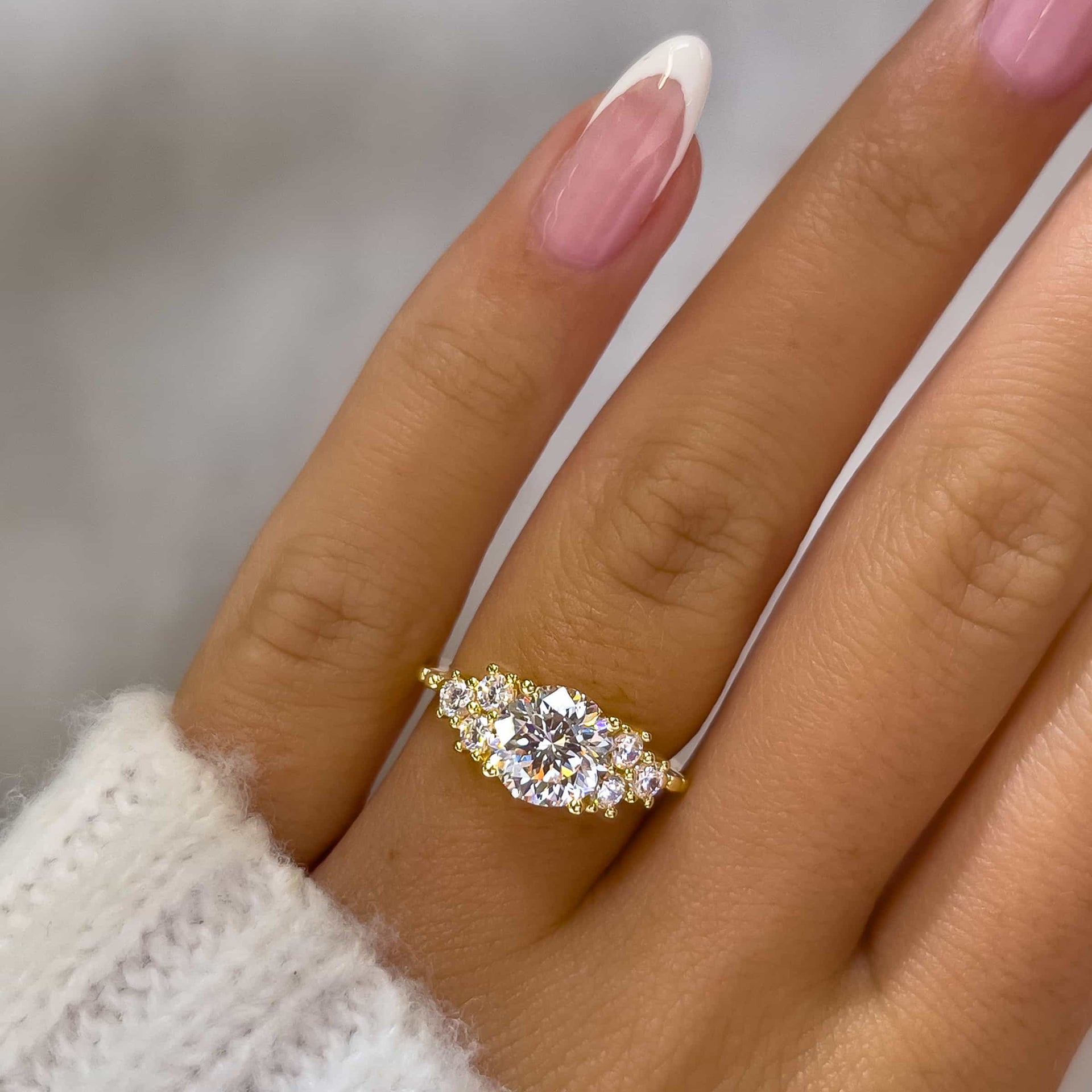 unique gold round cut engagement ring on model with french tip nails and white sweater