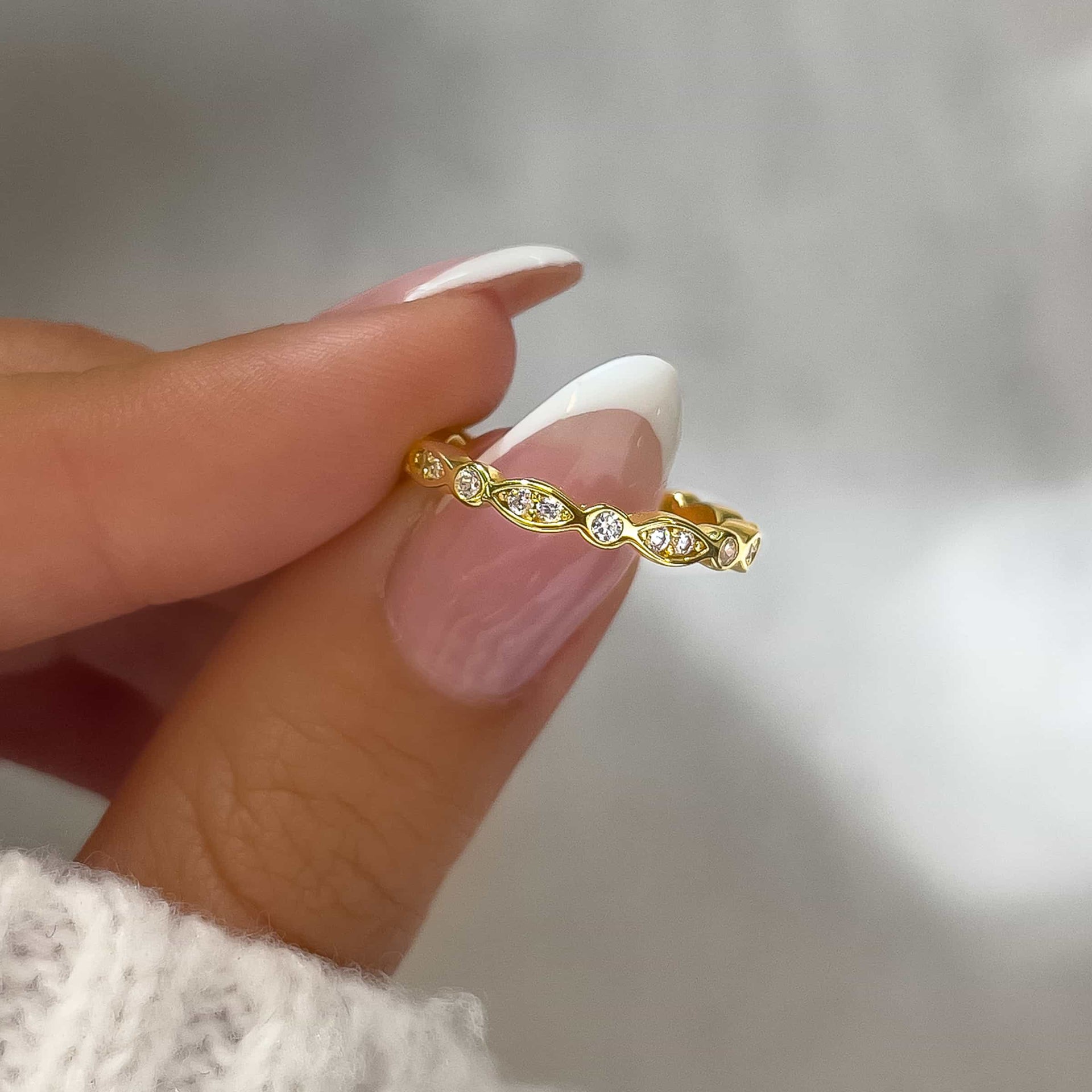 close up of gold vintage style eternity wedding band held by model with french tip nails and white sweater