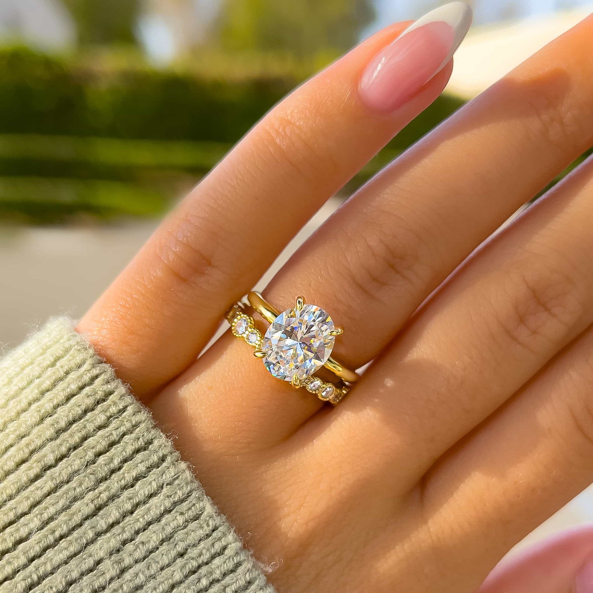 stunning gold wedding ring set made up of oval cut solitaire and unique multi-size stone wedding band on model with french tip nails