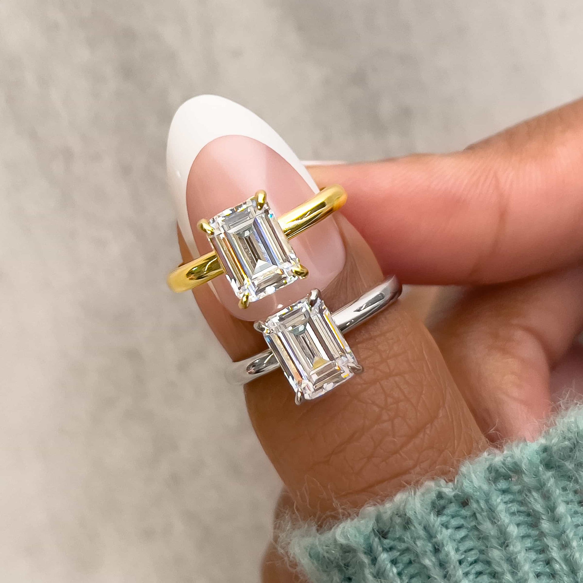 a 1.5 carat emerald cut solitaire engagement ring shown in gold and silver held by model with green sweater