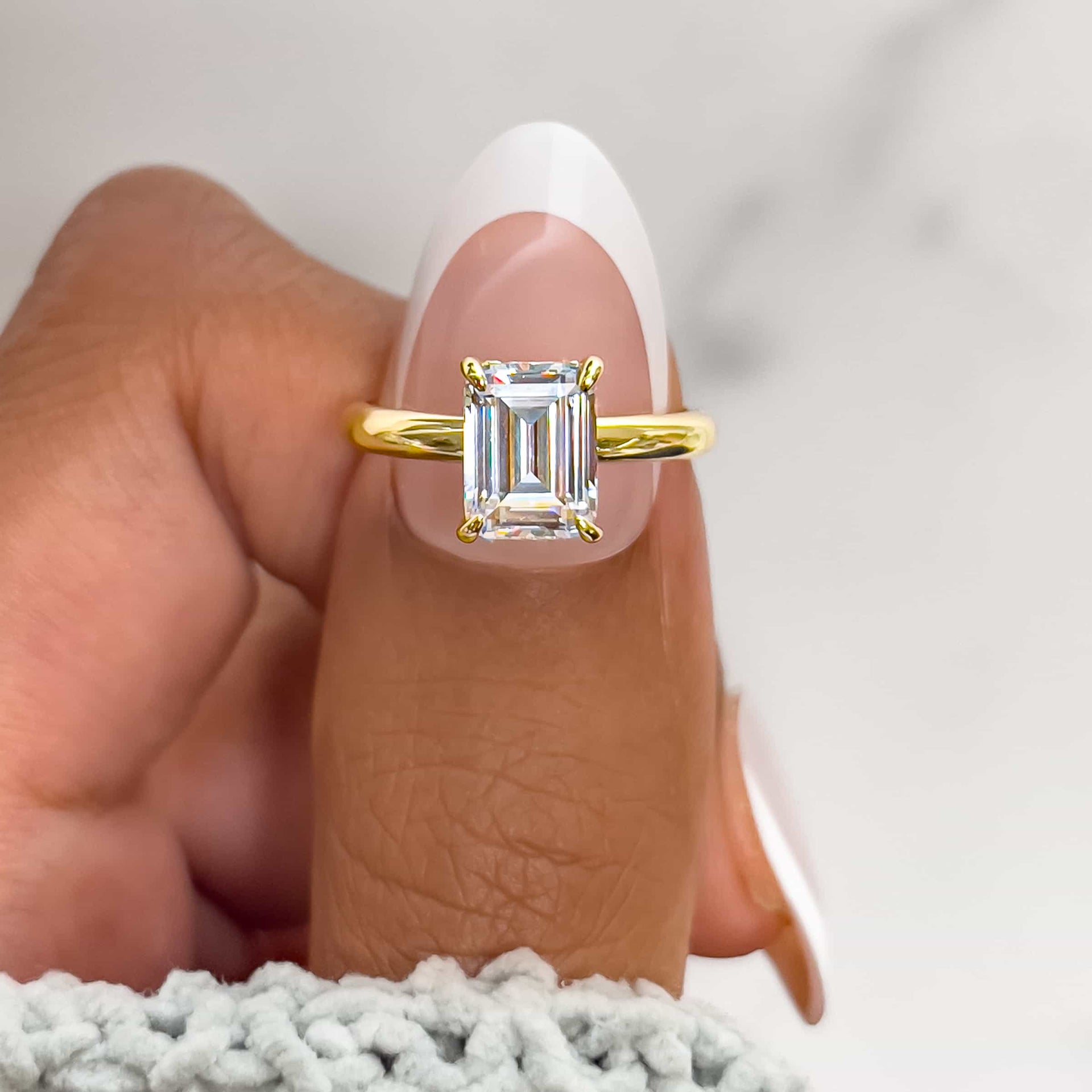 Gold 1.5 carat emerald cut engagement ring on model with french tip nails and white sweater