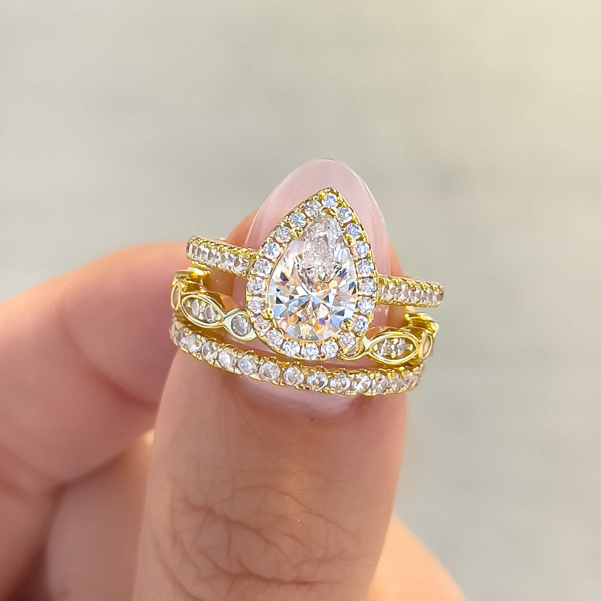 gold triple wedding ring stack held by model with neutral nails