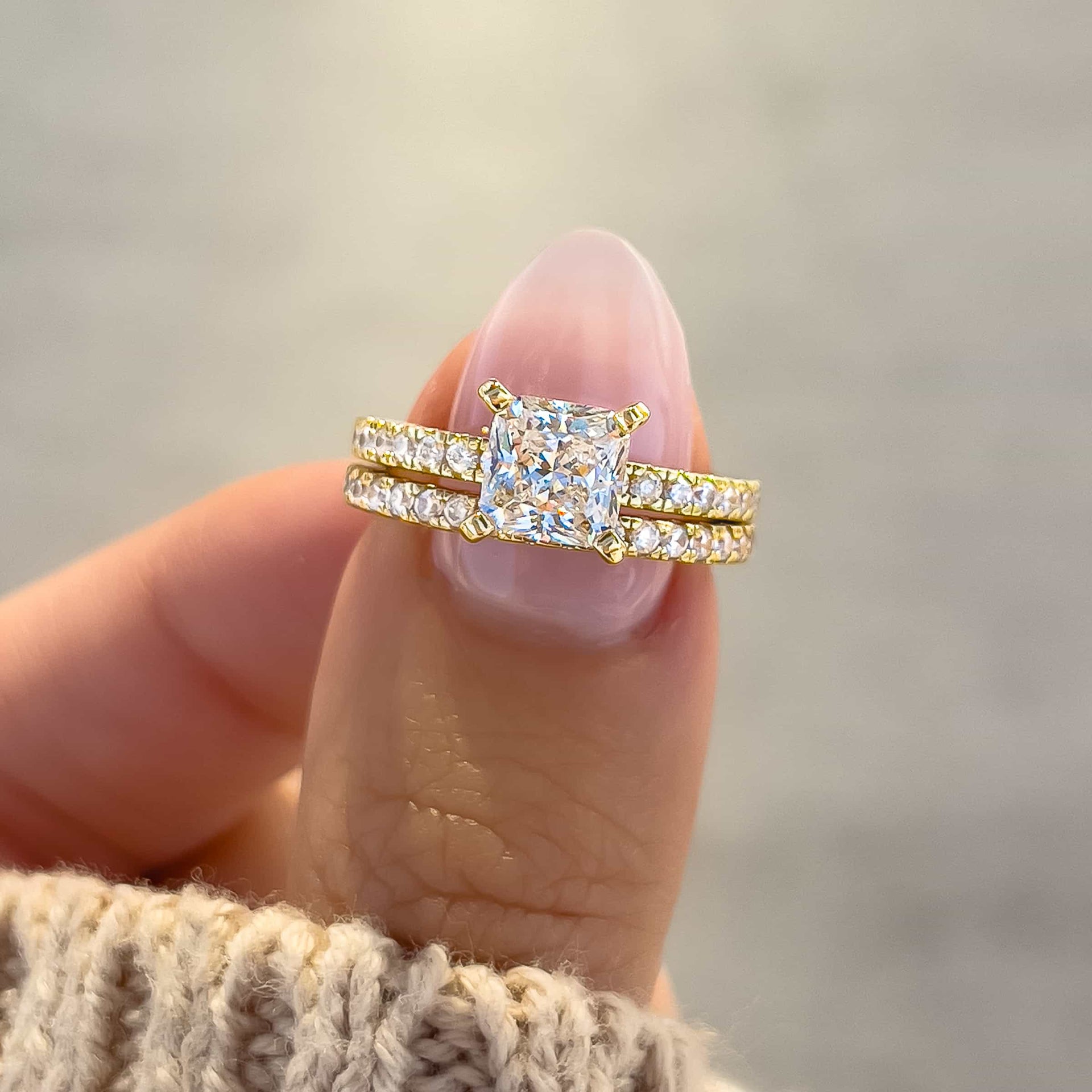 timeless gold princess cut wedding ring set held by model with light pink nails