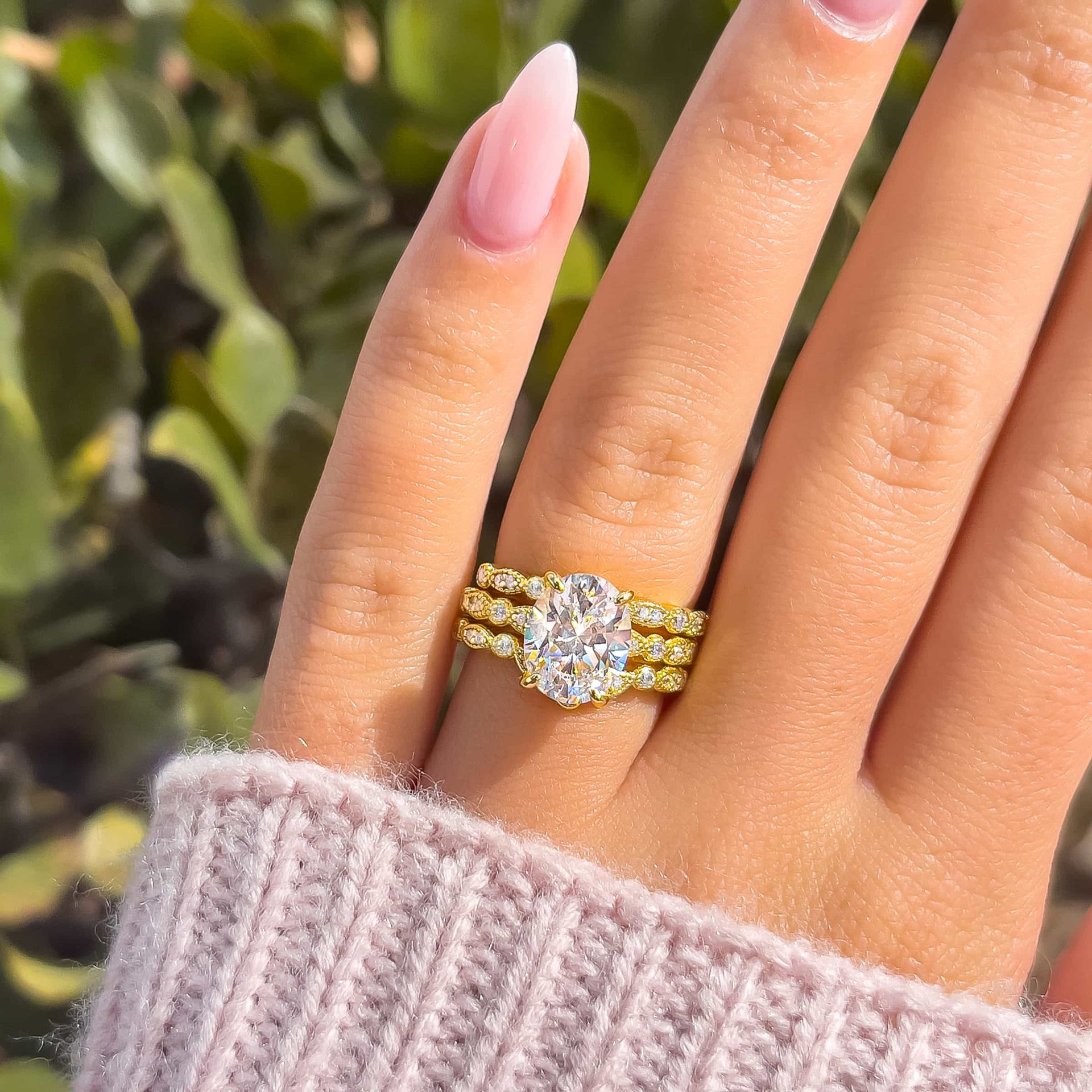 Gold 3 carat oval cut engagement ring with vintage half eternity detailing paired with two matching vintage half eternity band on model with light pink sweater and light pink nails