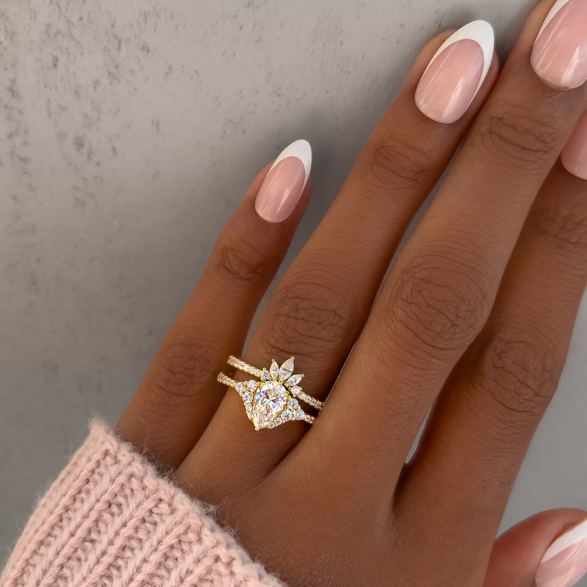 gold vintage 1 carat pear cut wedding ring set on model with french tip nails and pink knit sweater