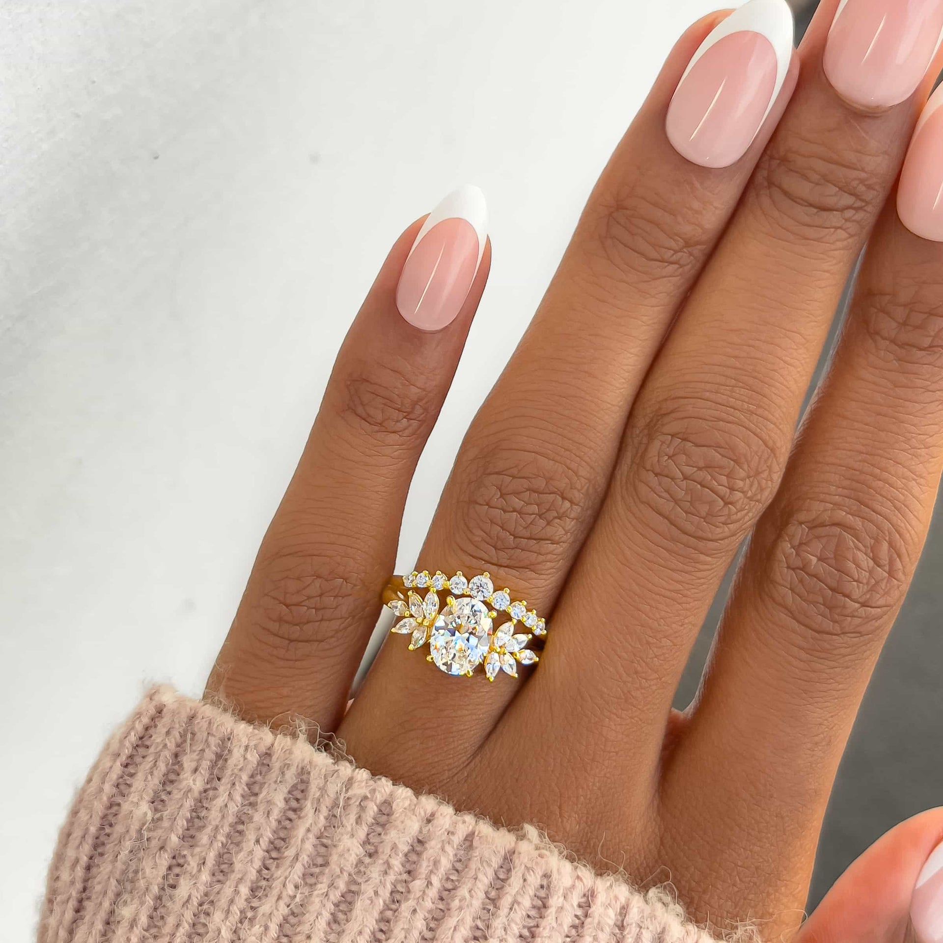 gold vintage 1 carat oval cut split shank engagement ring worn by model with french tip nails and neutral colored sweater