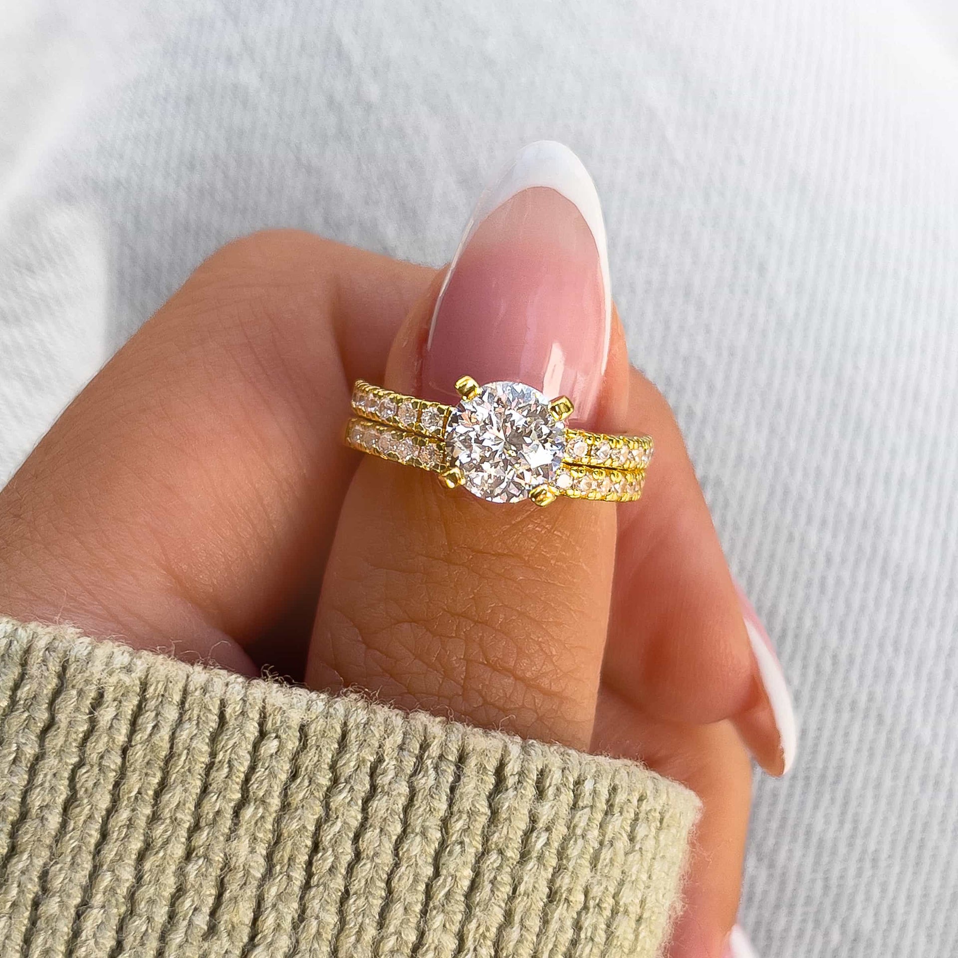 simple gold 1.75 carat round cut wedding ring set on model with french tip nails and tan sweater