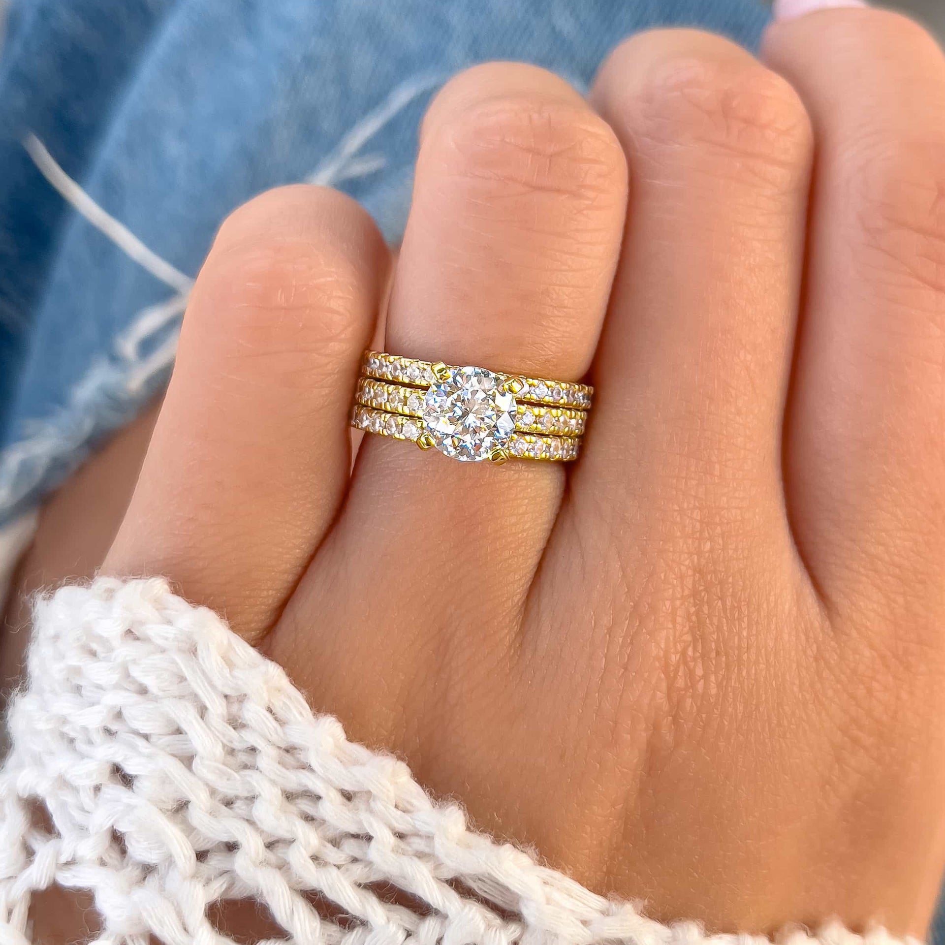 a gold triple wedding ring stack made up of round cut engagement ring and two matching half eternity wedding bands on model with white sweater