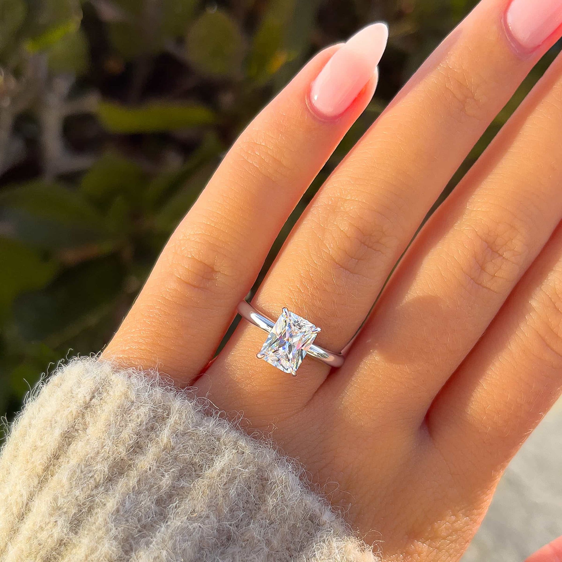 Silver radiant solitaire engagement ring on model with neutral nails and sweater